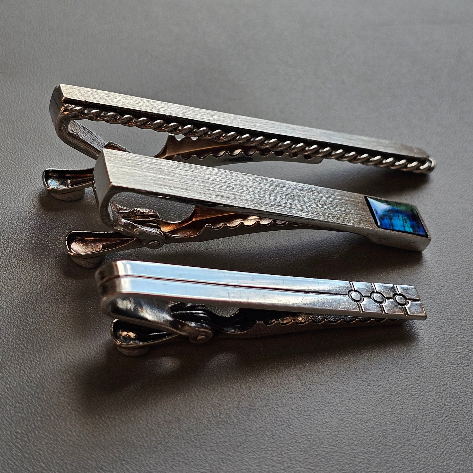 Stack of three metallic tie clips with different designs and textures.