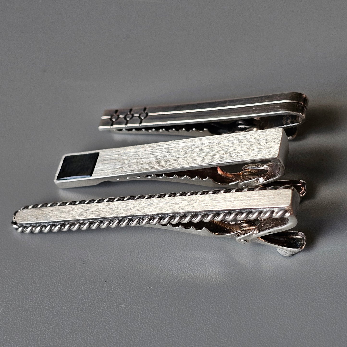 Set of three silver-toned metal tie clips with different textured designs.