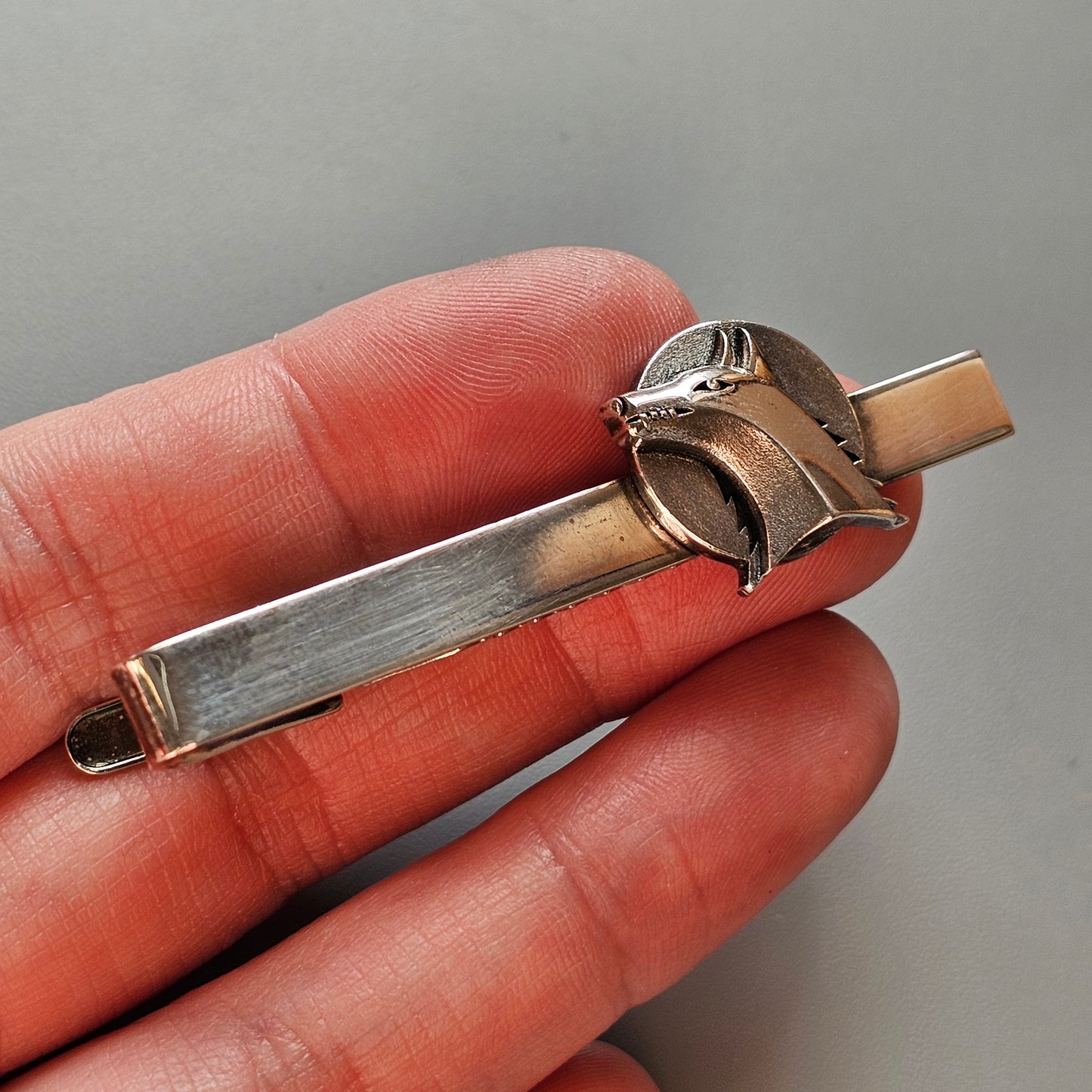 Metallic tie clip featuring a stylized football helmet design.