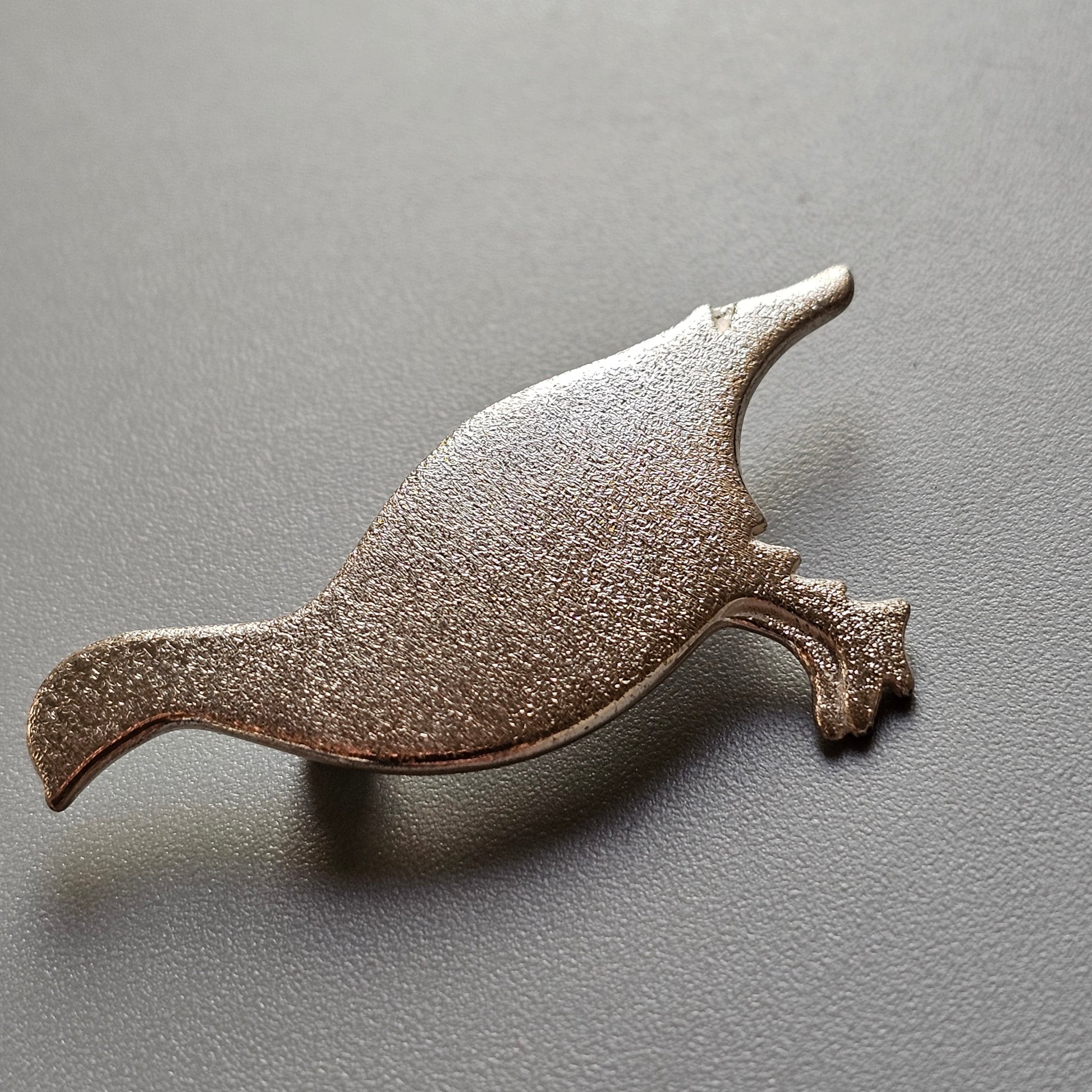 Metallic dolphin-shaped brooch or pin with a textured, glittery surface.