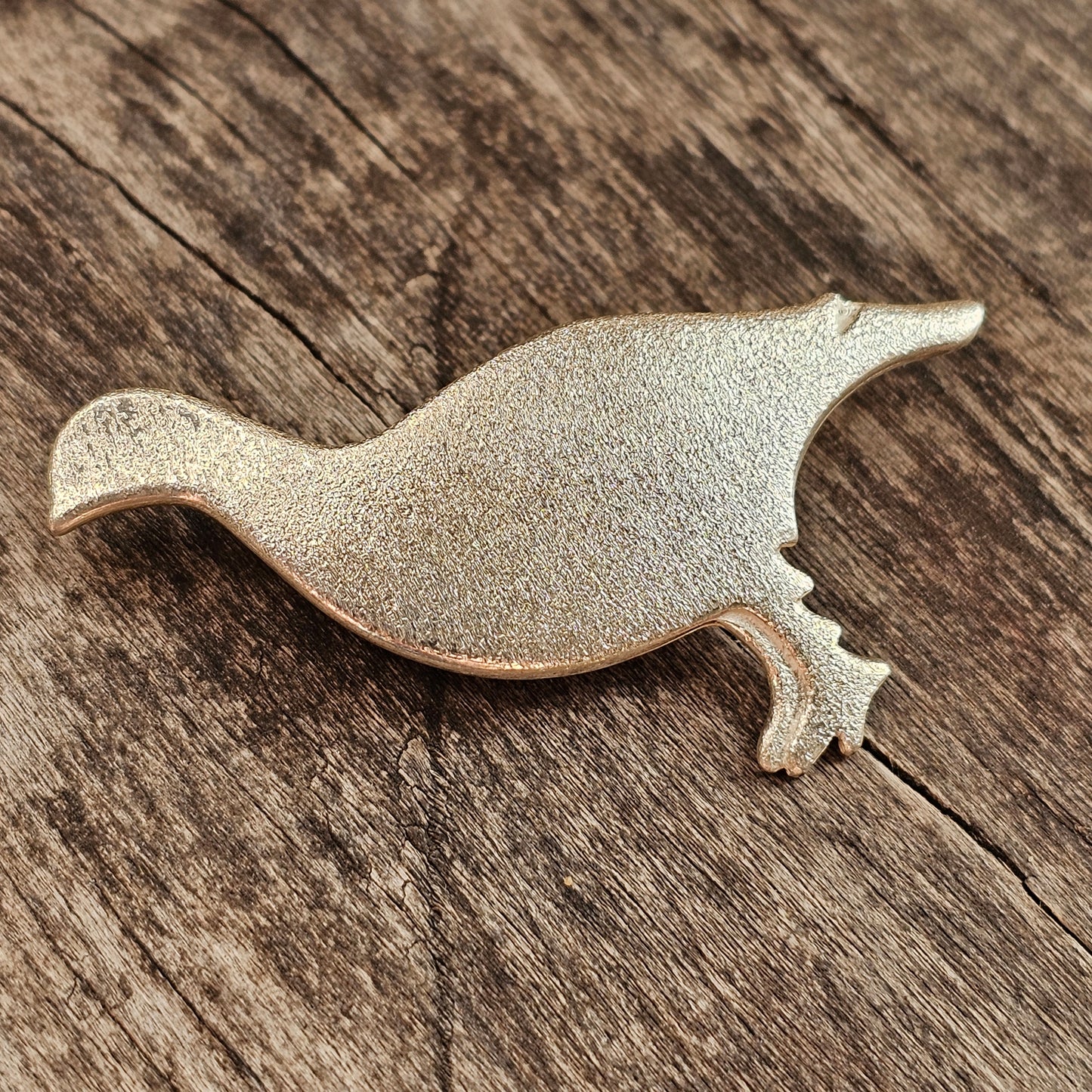 Metal bird-shaped brooch or pin with a textured surface.