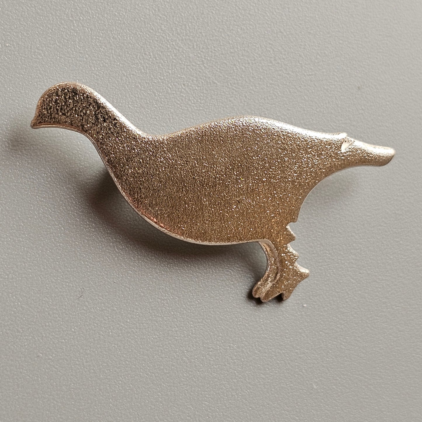 Metal pin or brooch in the shape of a stylized duck or goose.