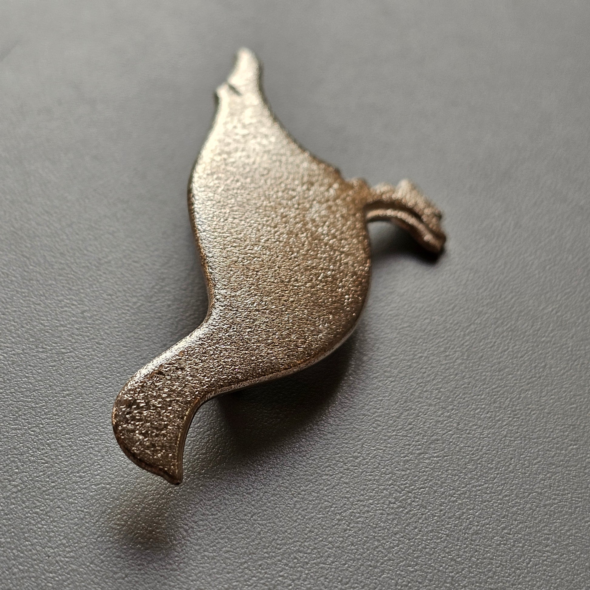 Metallic dove-shaped brooch or pin with a textured surface.