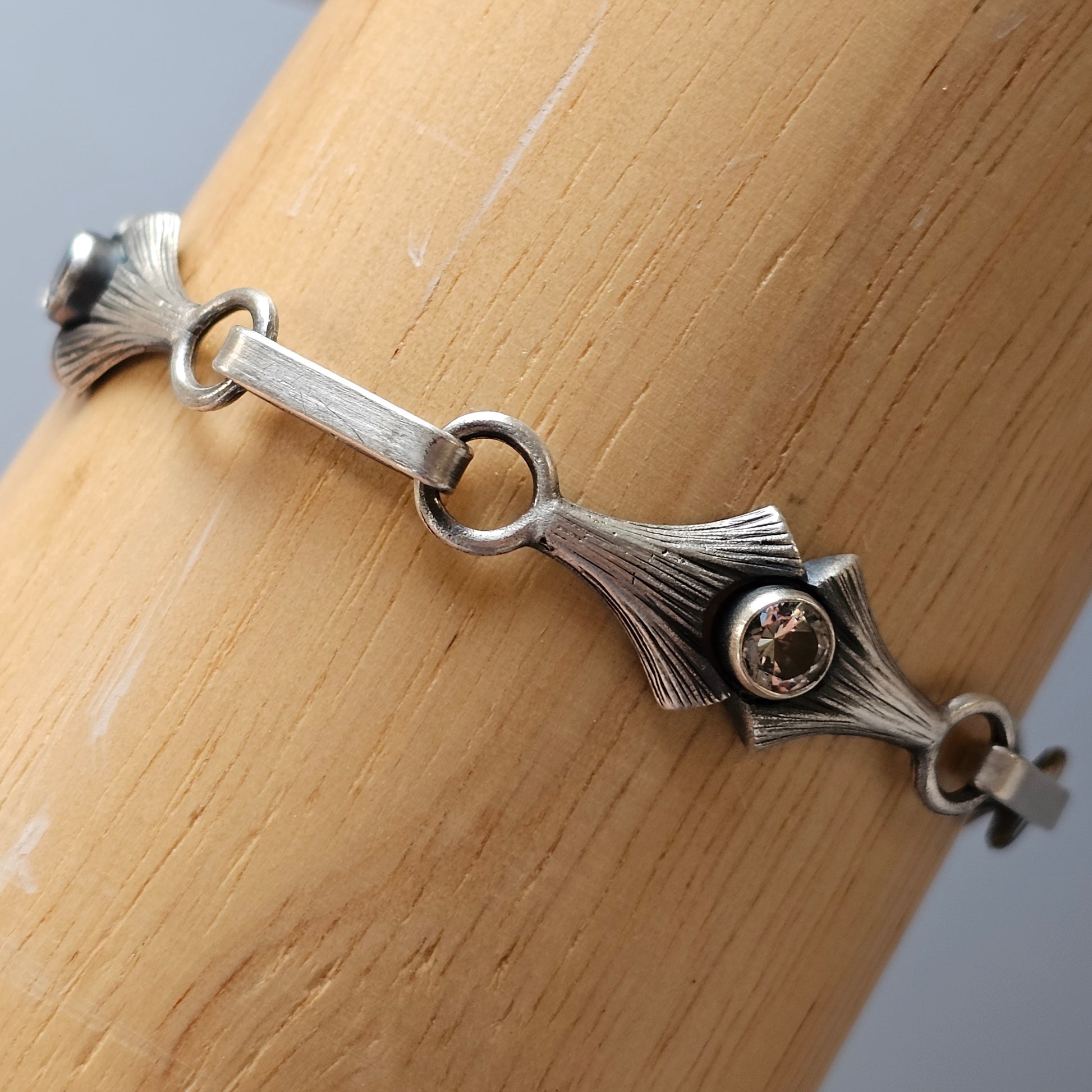 Silver bracelet with a central decorative element featuring a small gemstone.