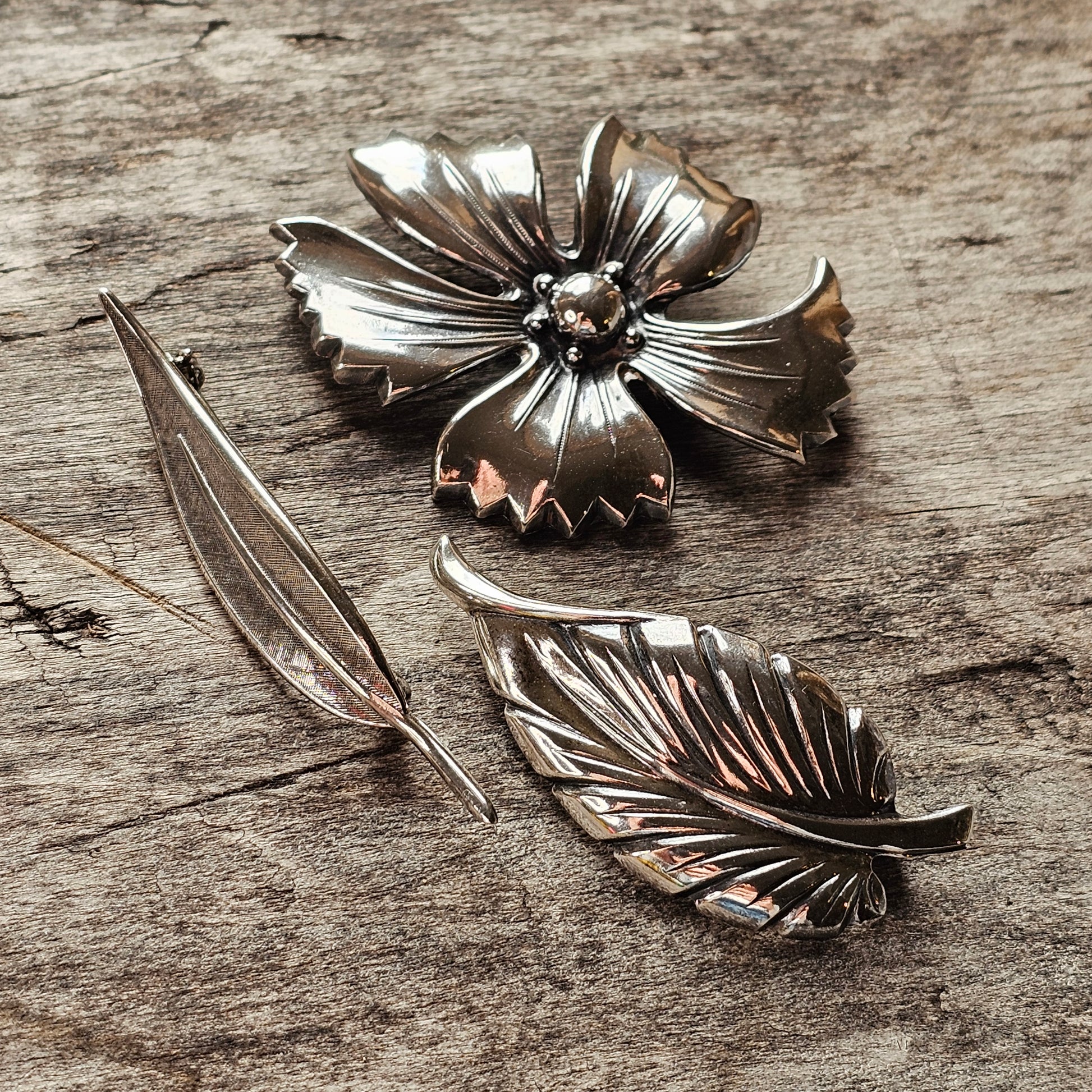 Metallic flower-shaped brooch or pin with separate leaf-like pieces.