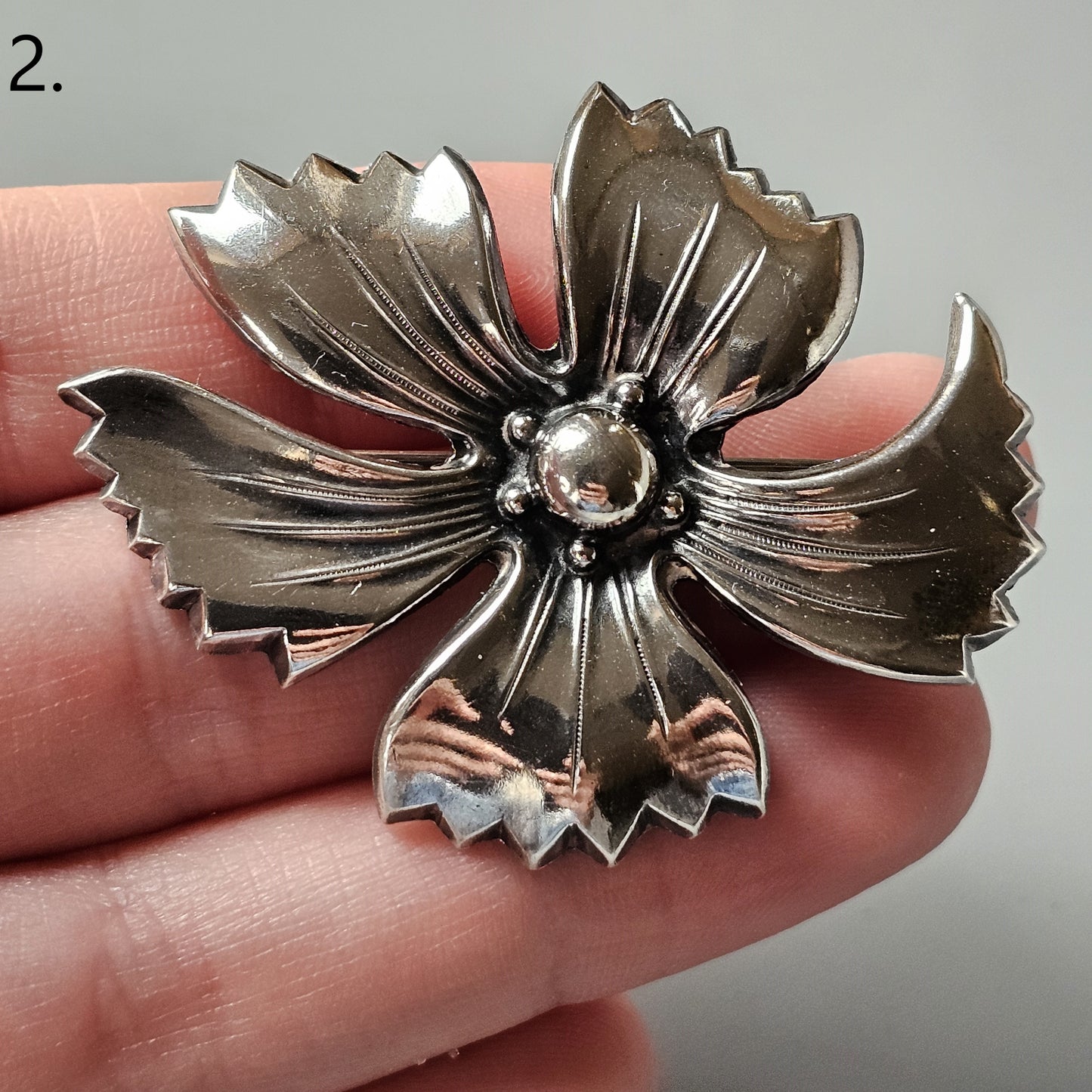 Ornate metal flower brooch with five pointed petals and a central bead.