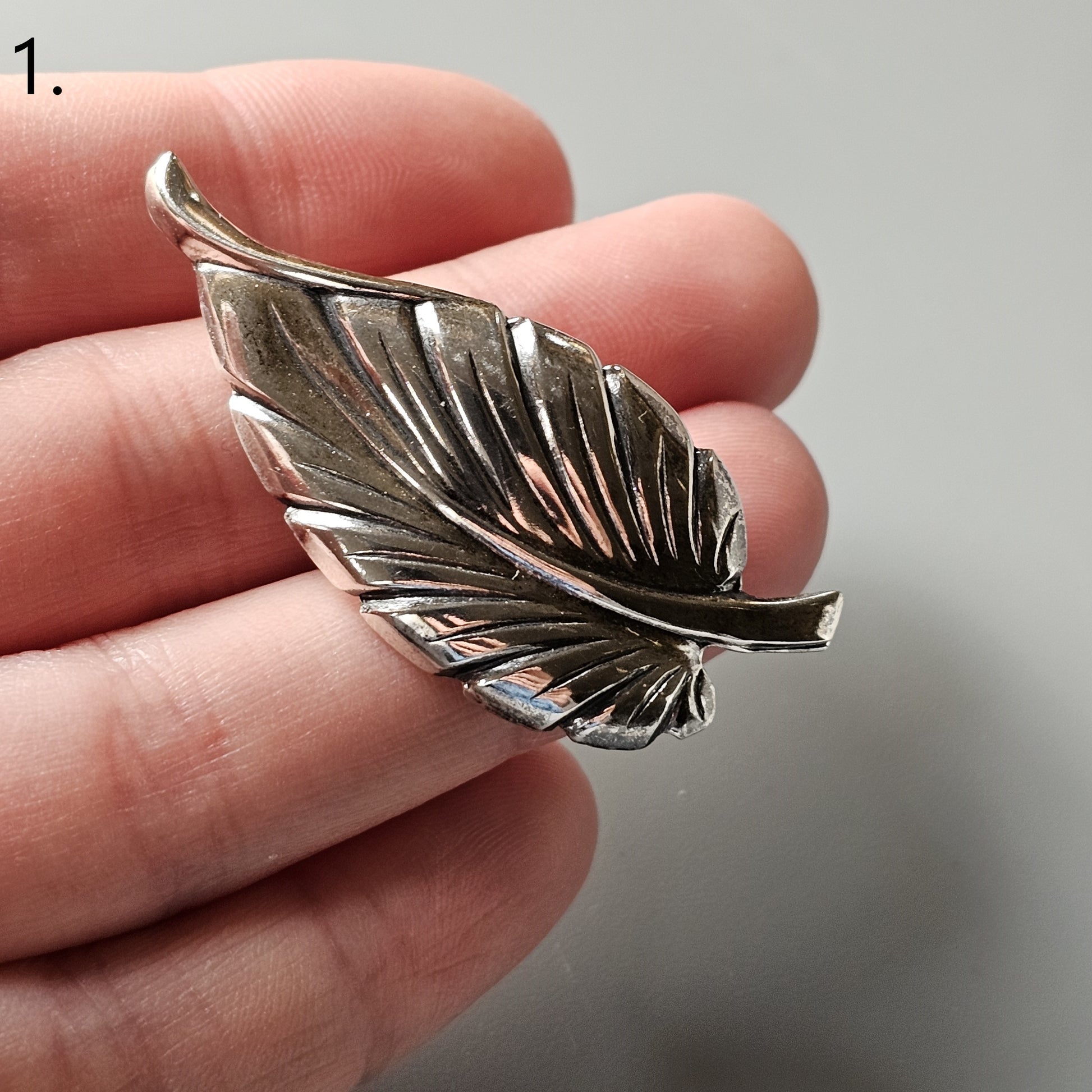 Silver leaf-shaped brooch or pendant with detailed vein patterns.