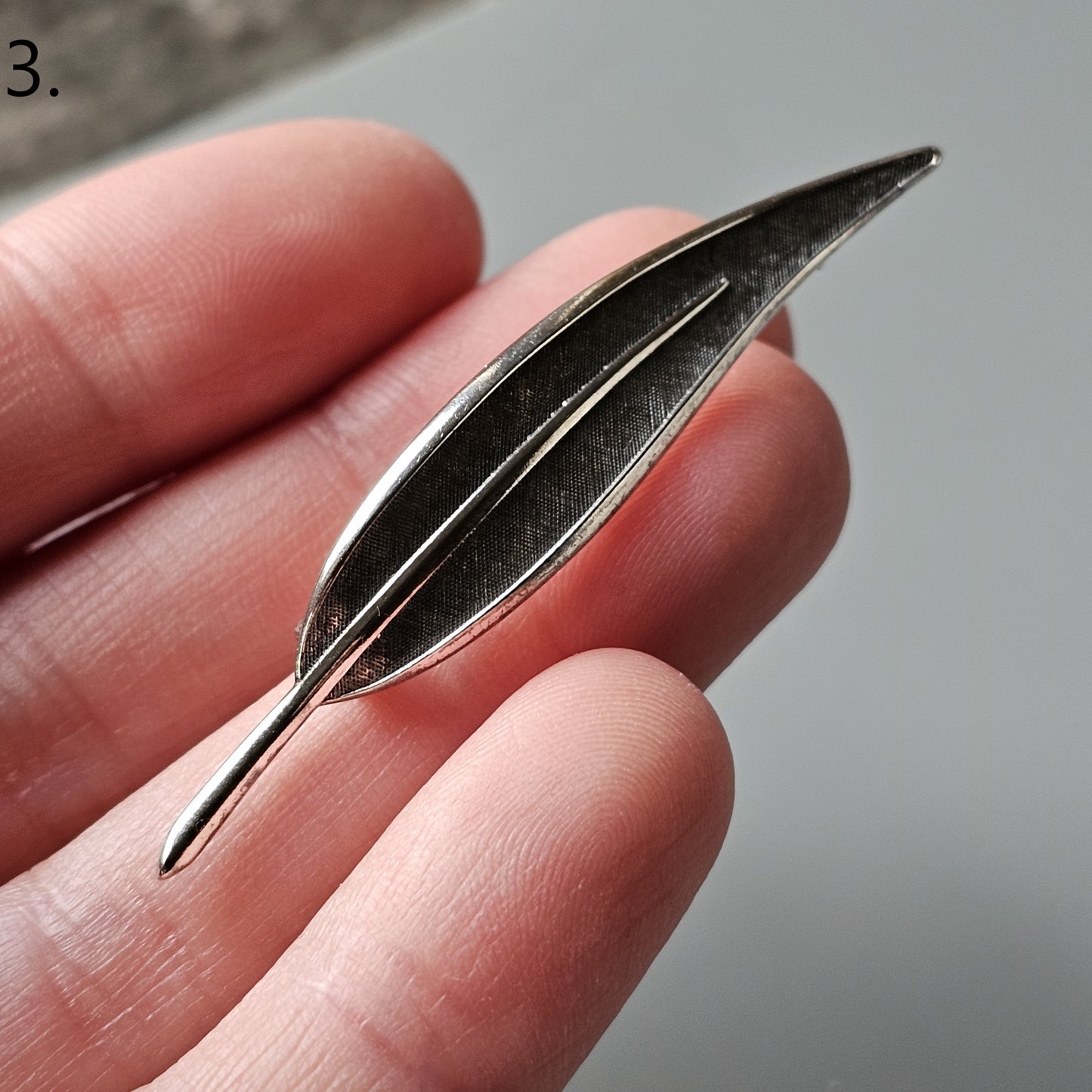 Silver metallic feather-shaped pin or brooch.