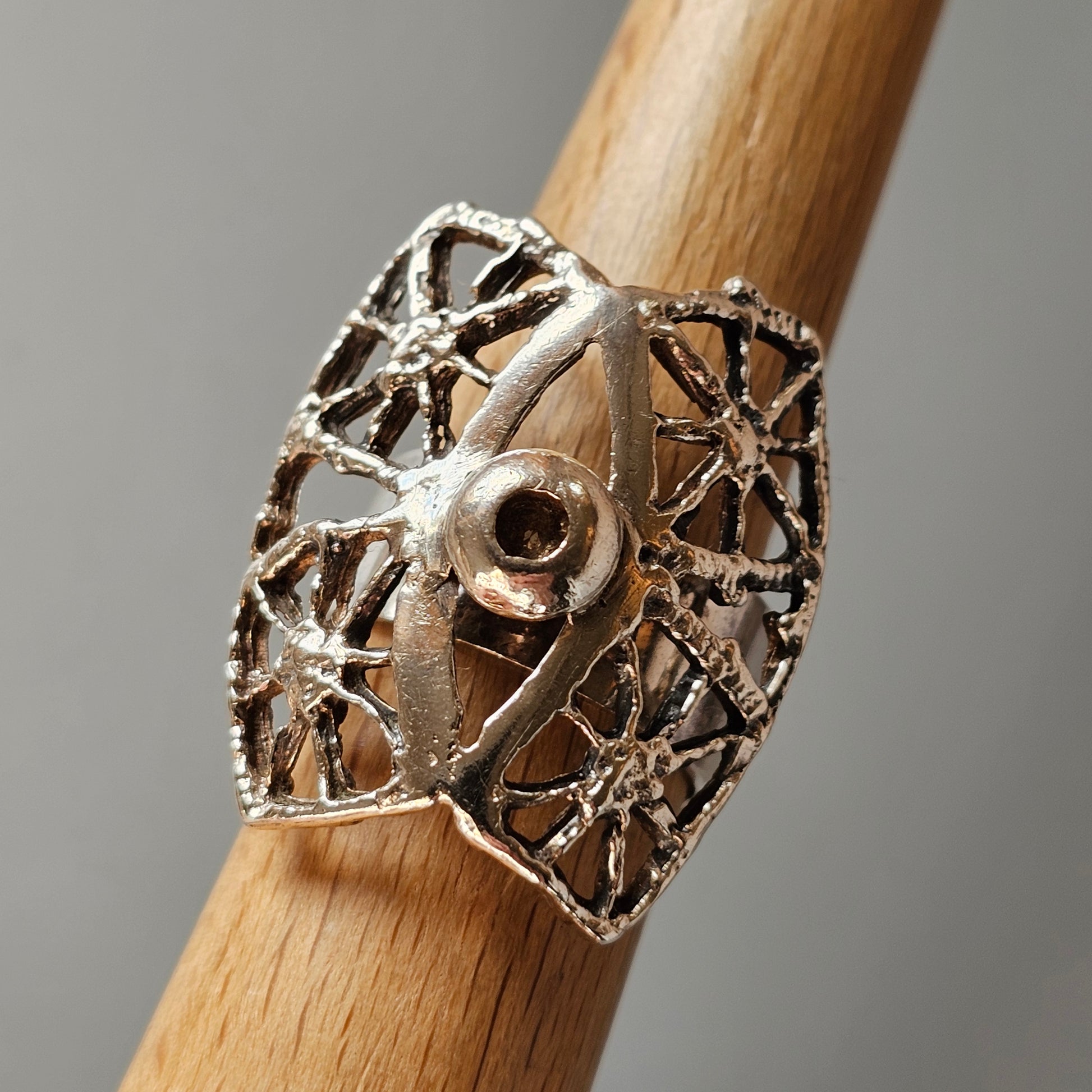 Intricate silver ring with a web-like design featuring a central eye motif.