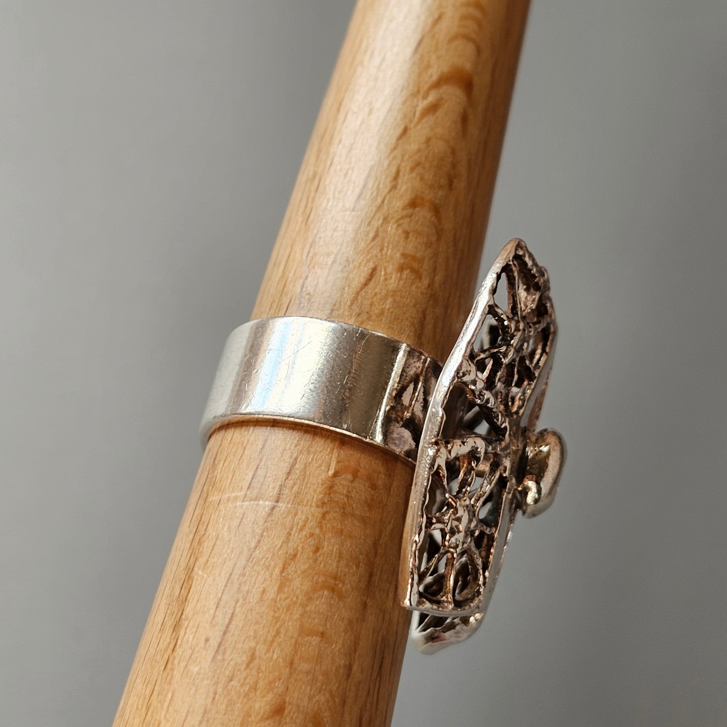 Ornate silver ring with an elongated filigree design on a wooden surface.