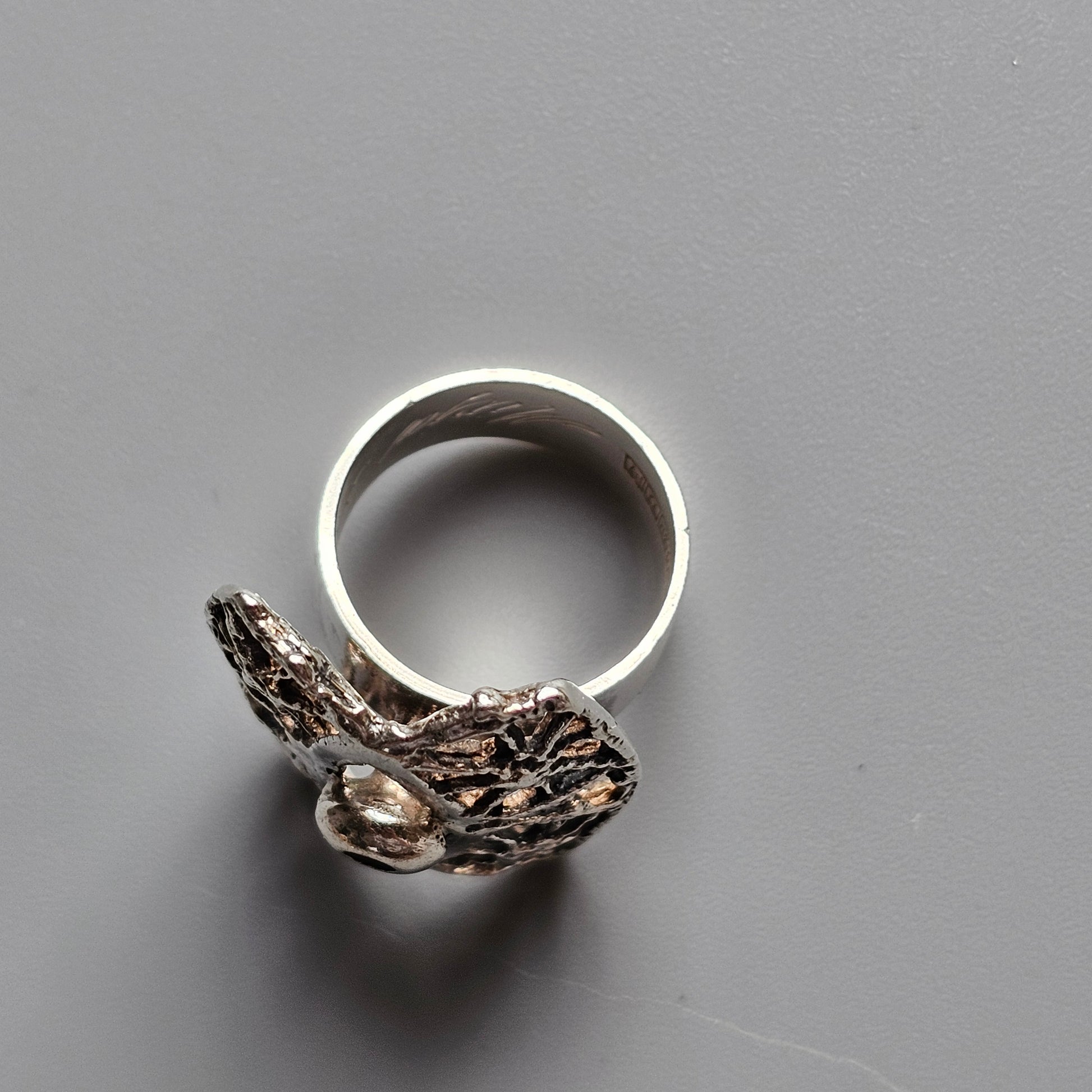 Silver ring with an intricate bird-shaped design attached to the band.