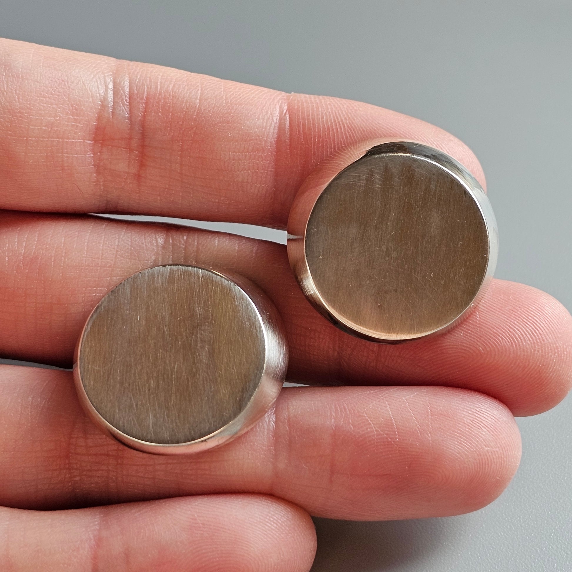 Two circular metal discs held in a person’s hand.