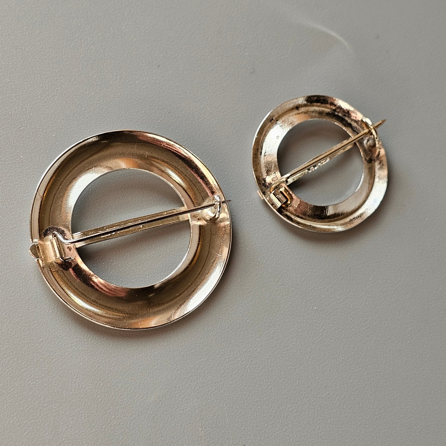 Two circular gold-toned brooches with bar pins across their centers.