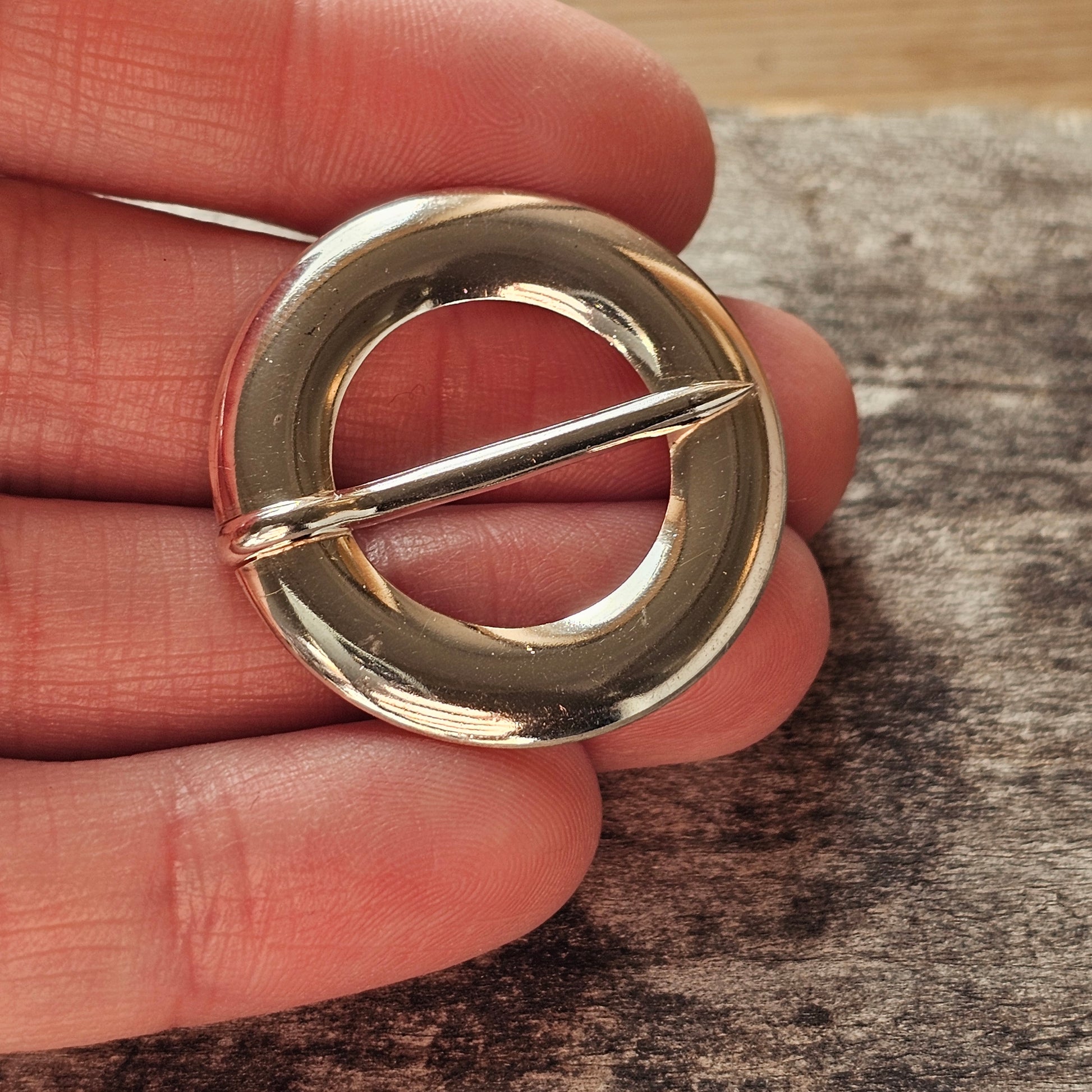 Circular metal brooch or pin with a diagonal bar across its center.