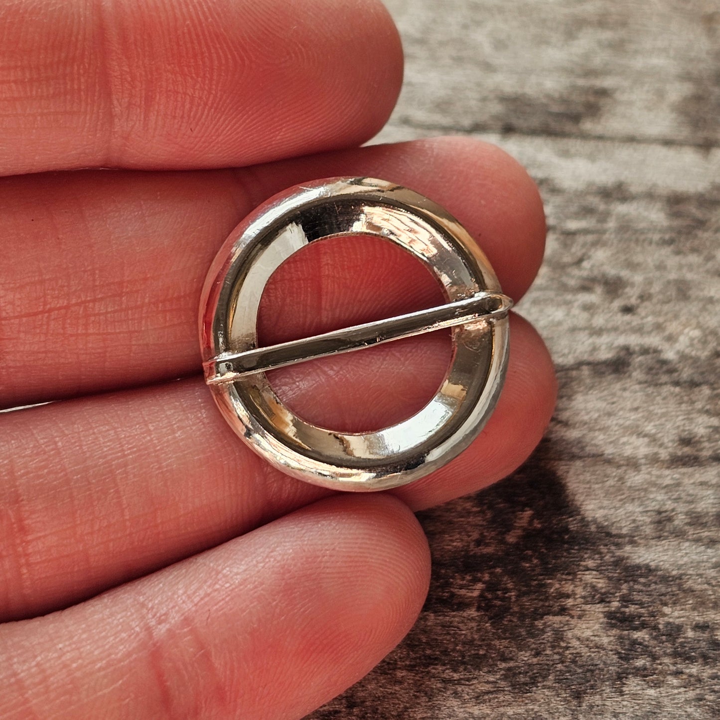 Circular silver brooch or pin with a horizontal bar across its center.