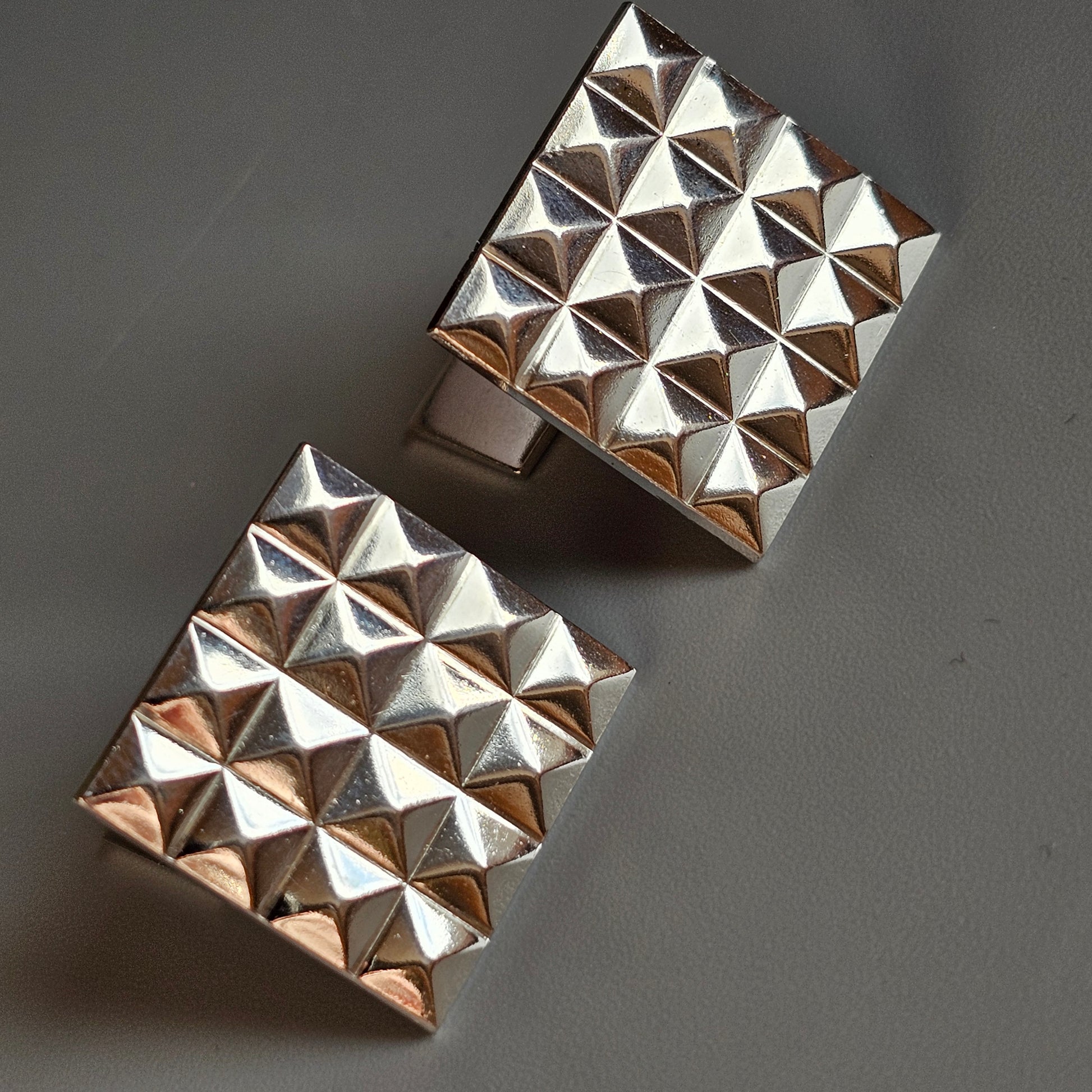 Pair of metallic cuff bracelets with pyramid-shaped studs covering their surfaces.