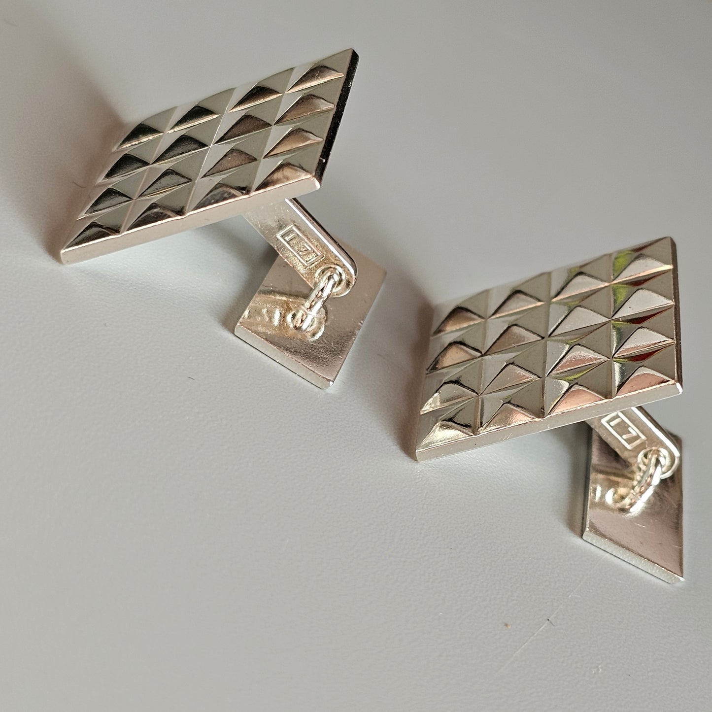 Pair of silver geometric cufflinks with textured triangular patterns.