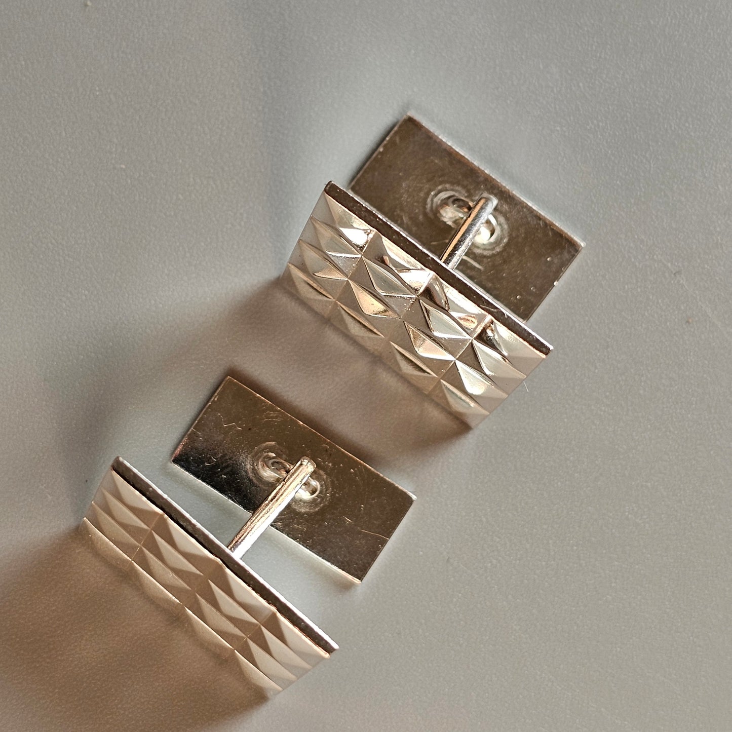 Pair of silver cufflinks with textured rectangular designs.