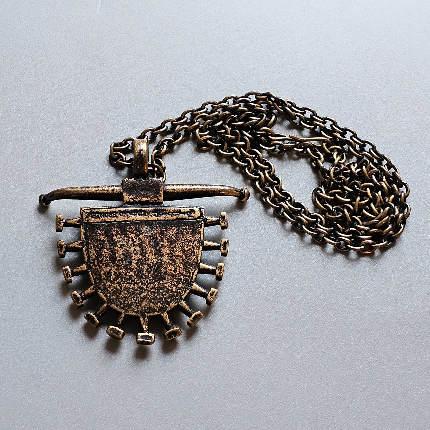 Antique-looking bronze pendant necklace with a shield-shaped design and decorative elements.