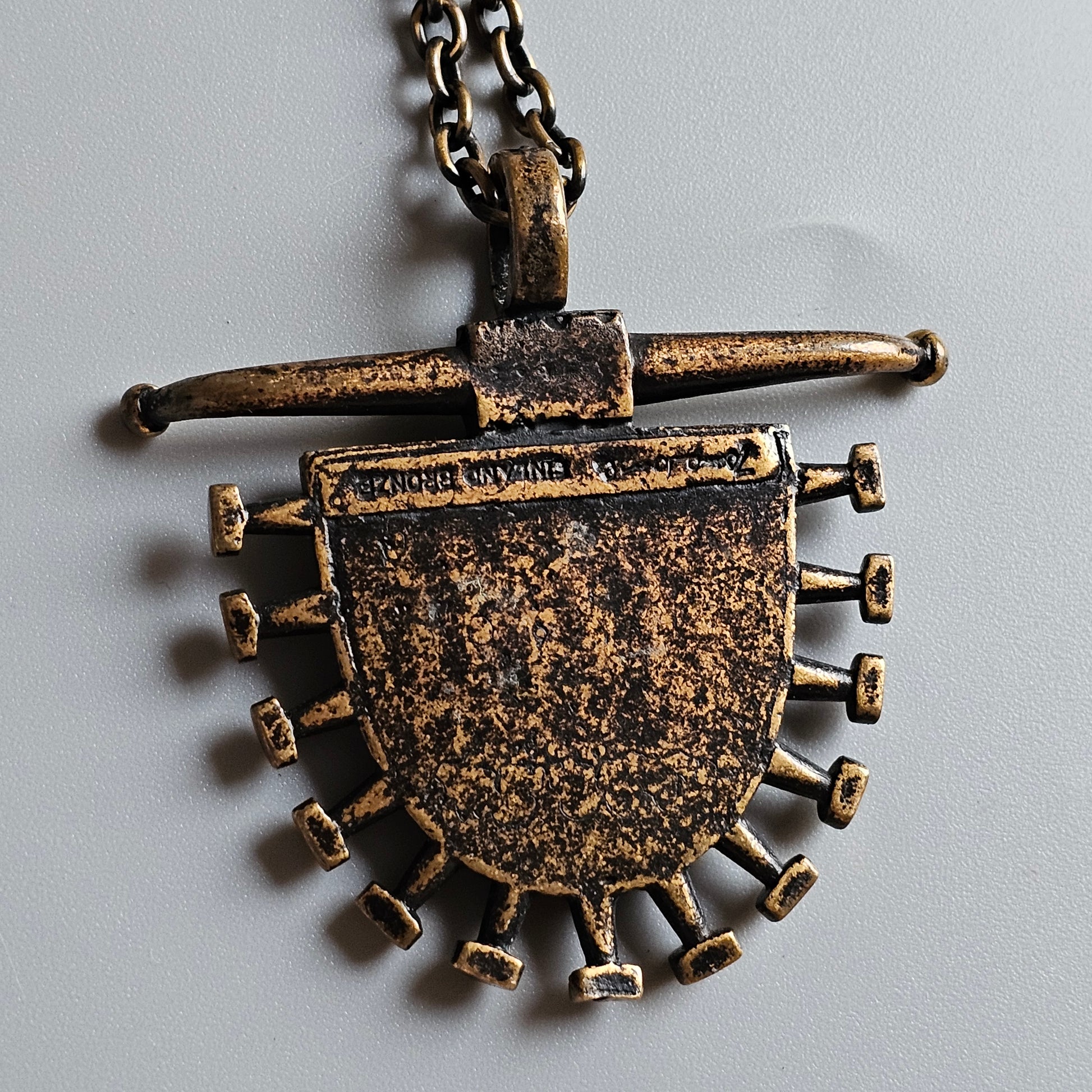 Ancient-looking metal pendant with a semicircular base adorned with protruding spikes and a crossbar at the top.