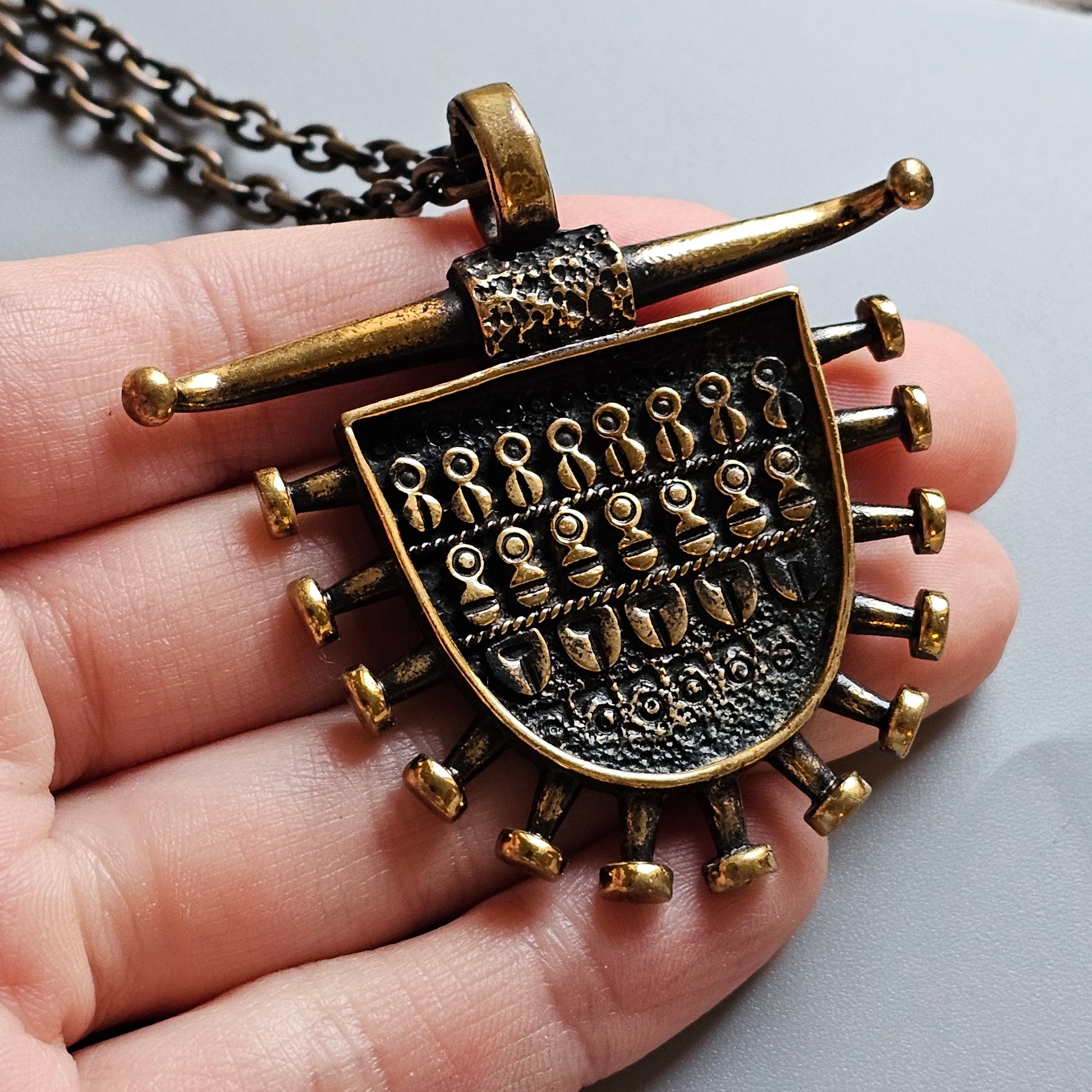 Ornate bronze pendant necklace with an intricate shield-like design and protruding spikes.