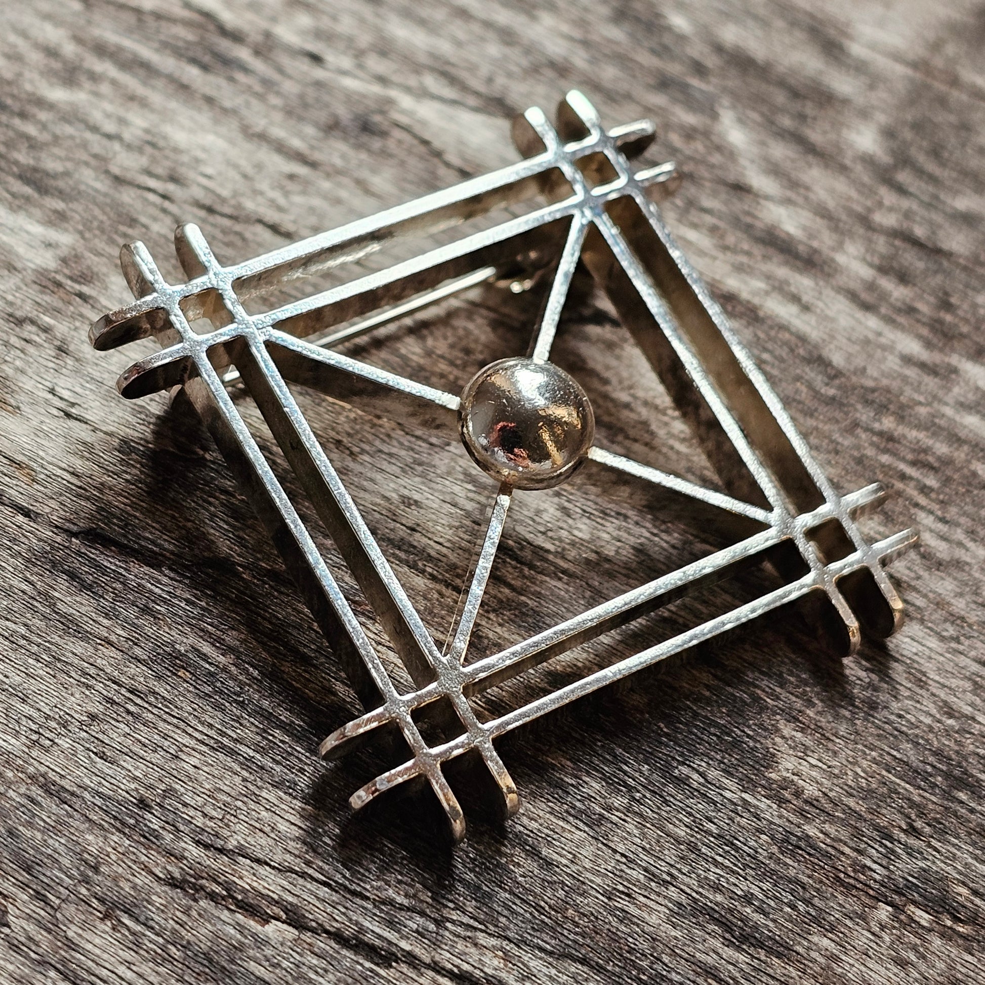 Geometric silver brooch or pendant with a square frame and central sphere.