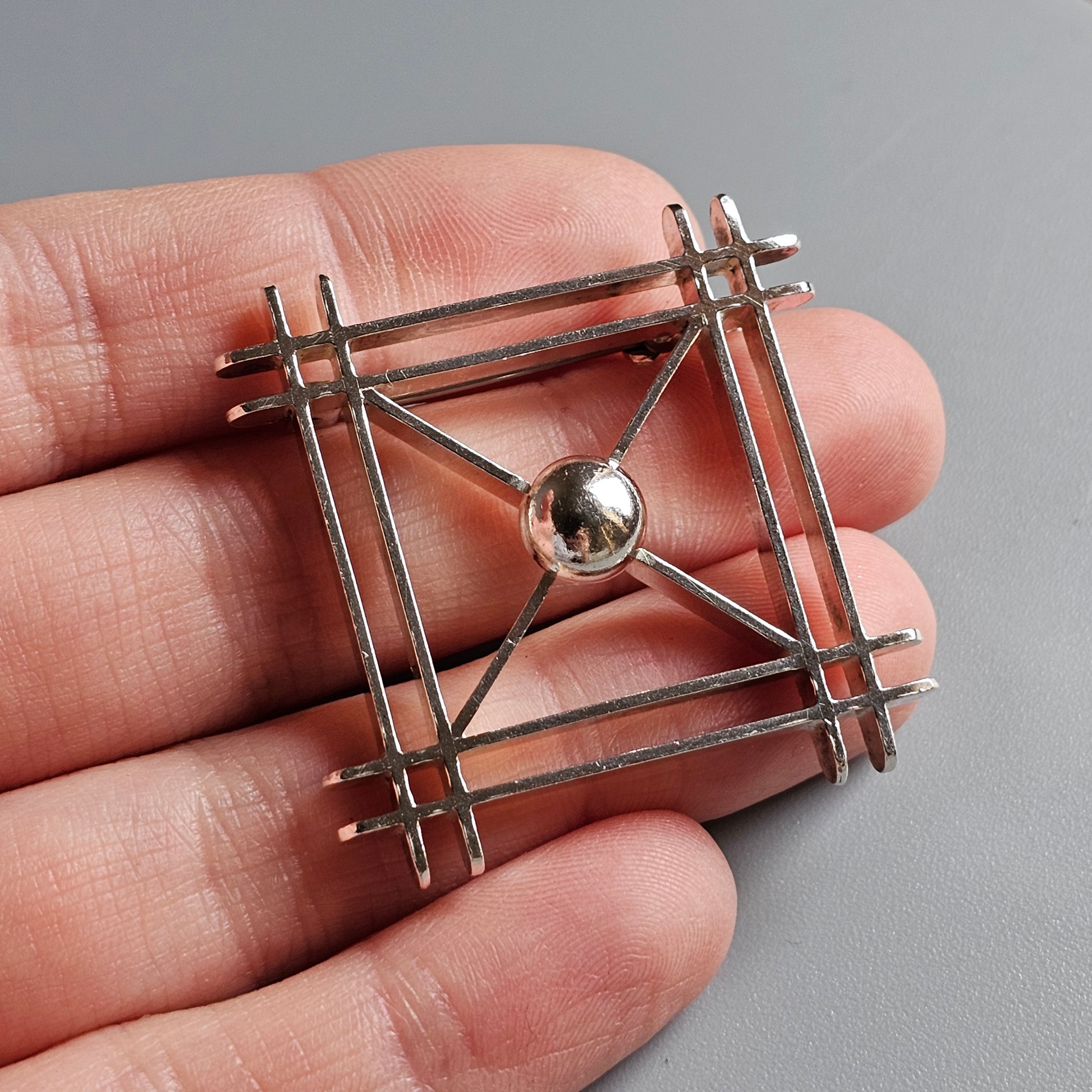 Geometric metal brooch or pendant with intersecting bars and a central sphere.