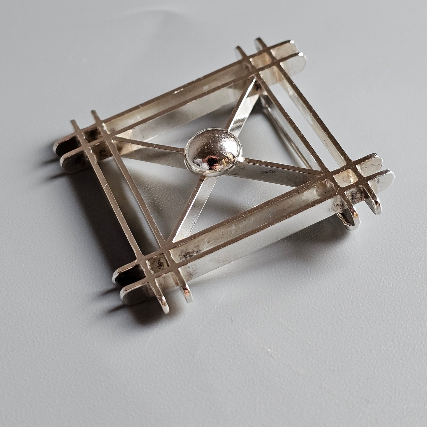 Geometric brooch or pin made of intersecting metal bars with a central circular element.