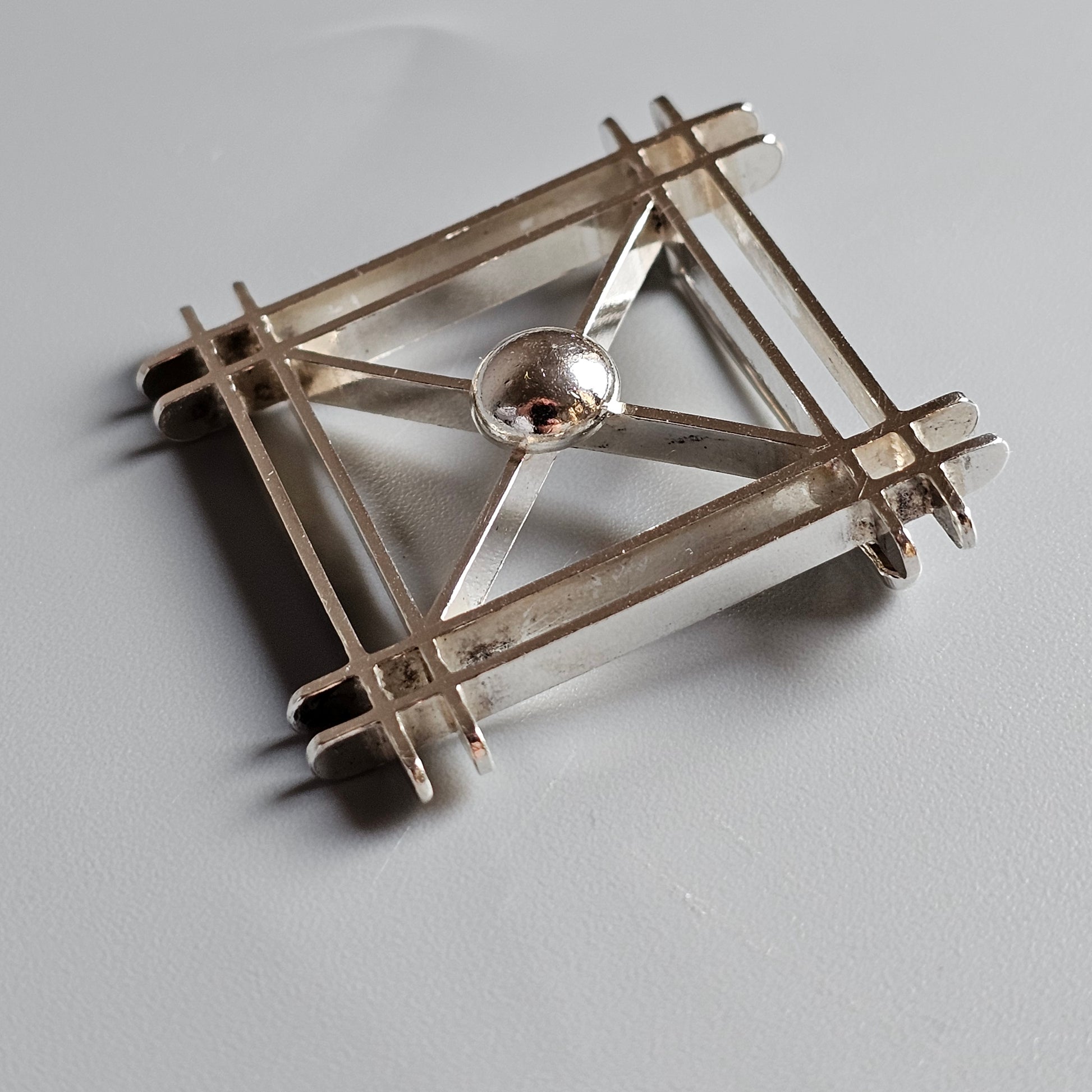 Geometric brooch or pin made of intersecting metal bars with a central circular element.