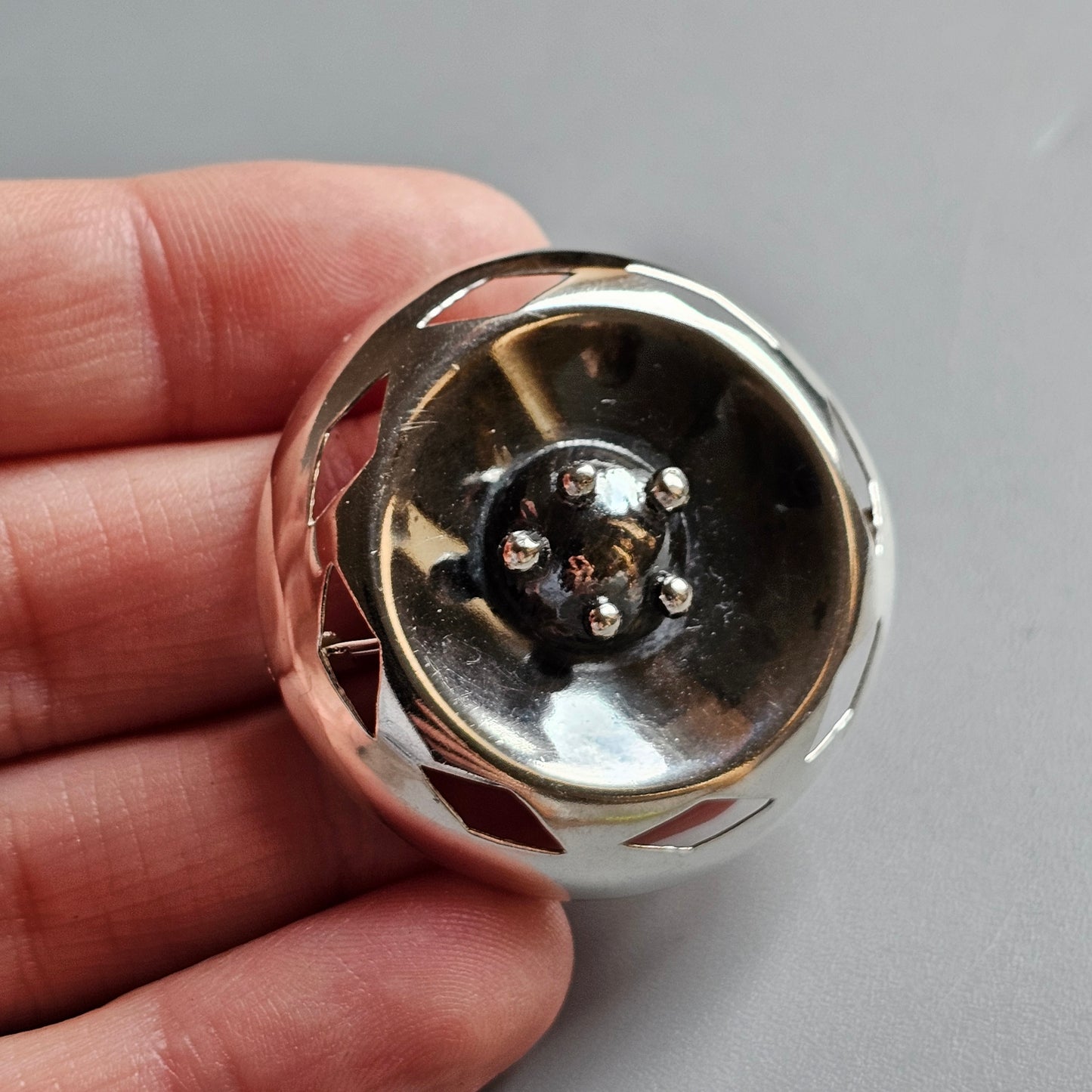 Metal spherical object with a reflective surface and small protruding elements in its center.