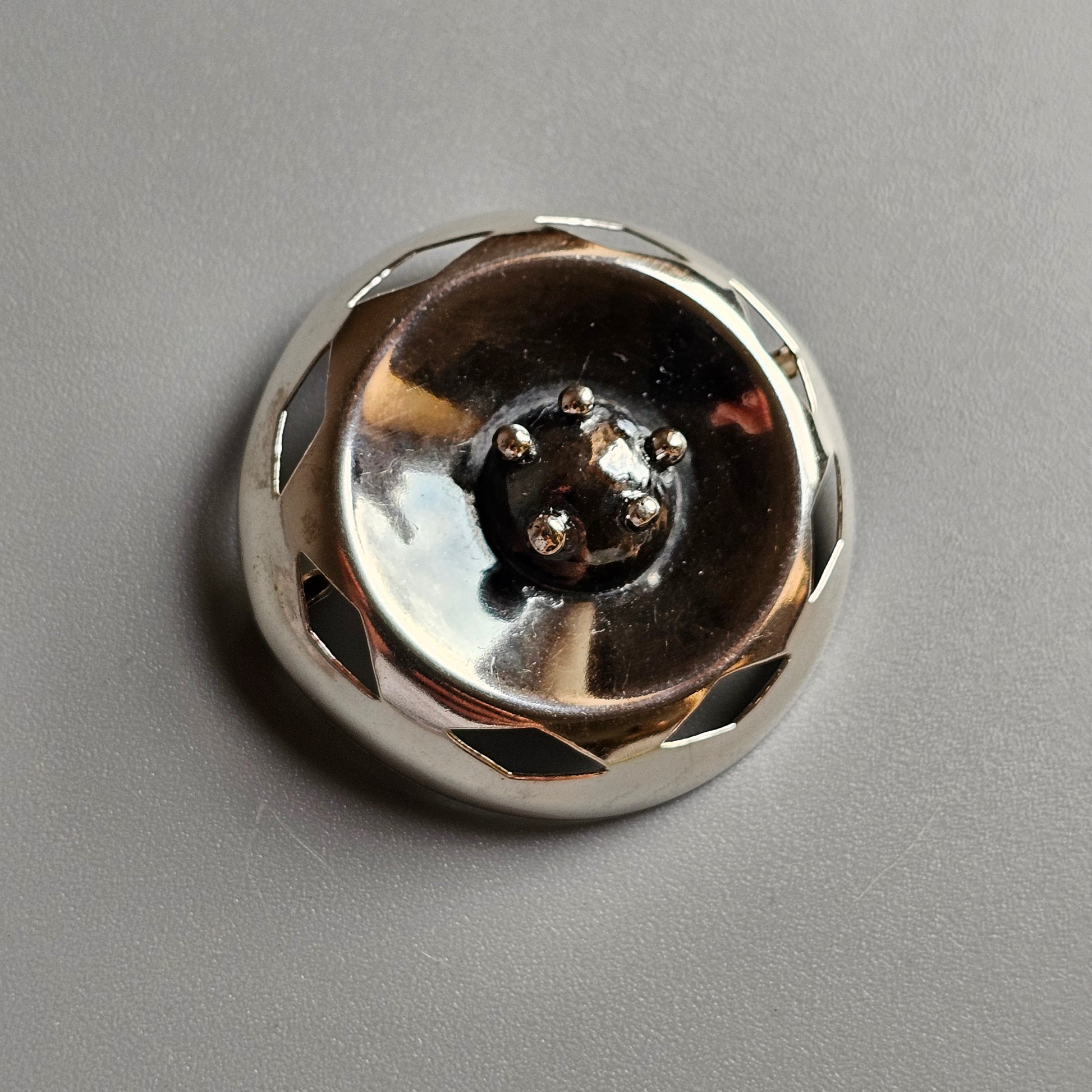 Shiny metallic button or knob with a faceted, reflective surface.