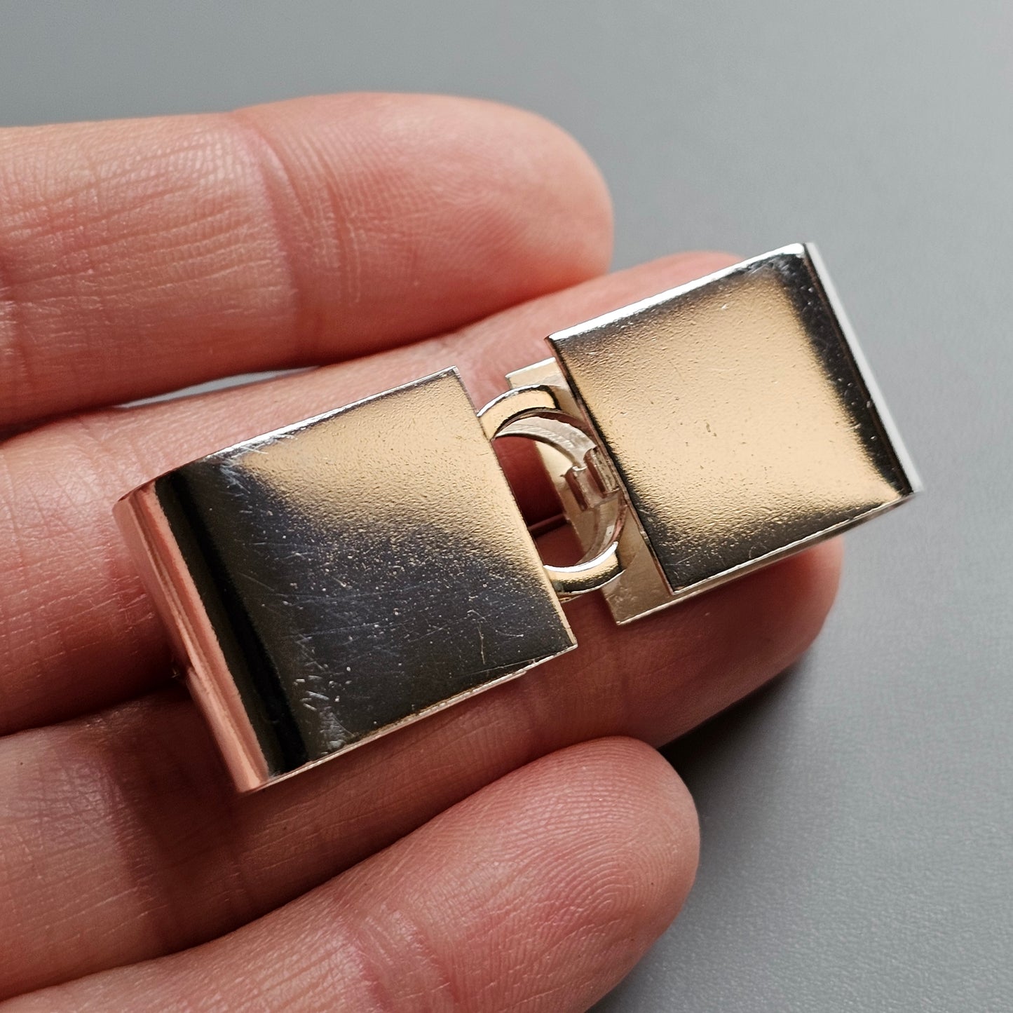 Metallic rectangular clasp or fastener with two hinged parts.