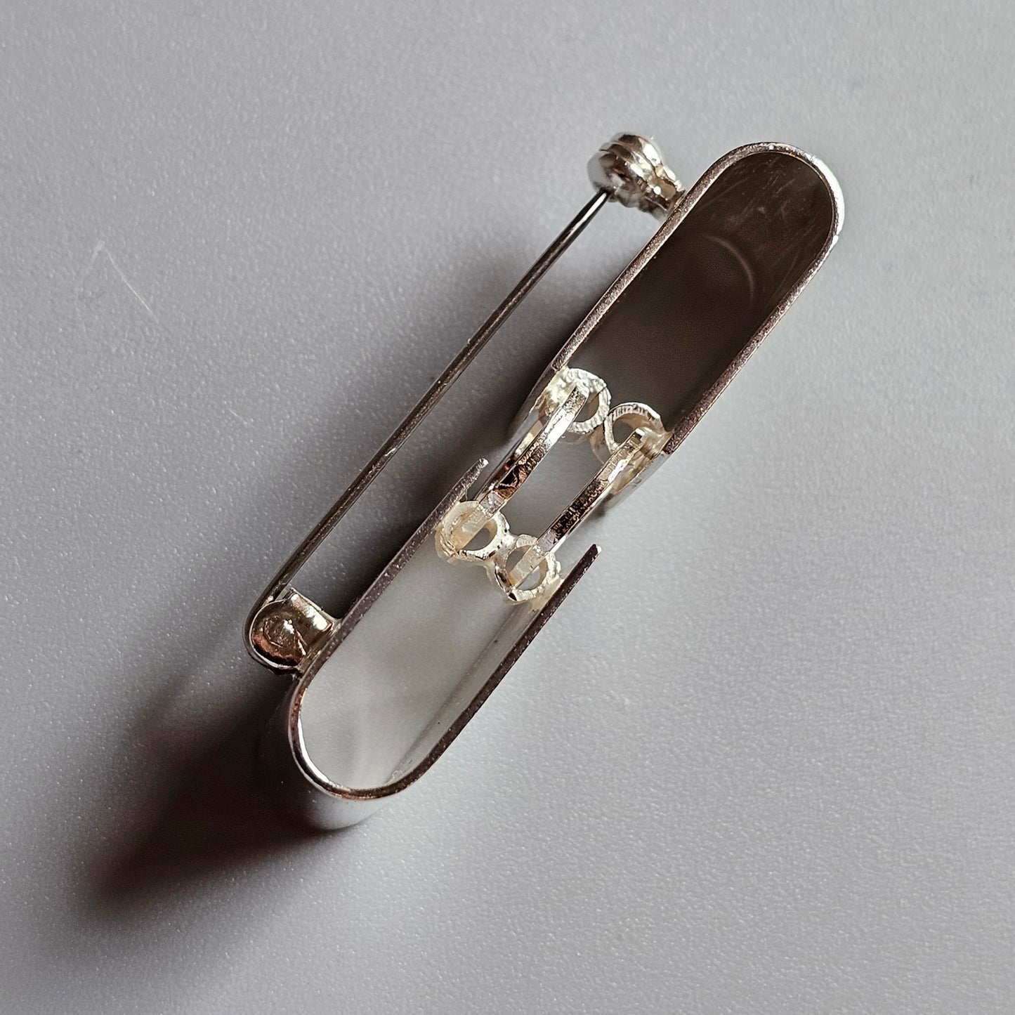 Silver safety pin with decorative elements on its clasp.