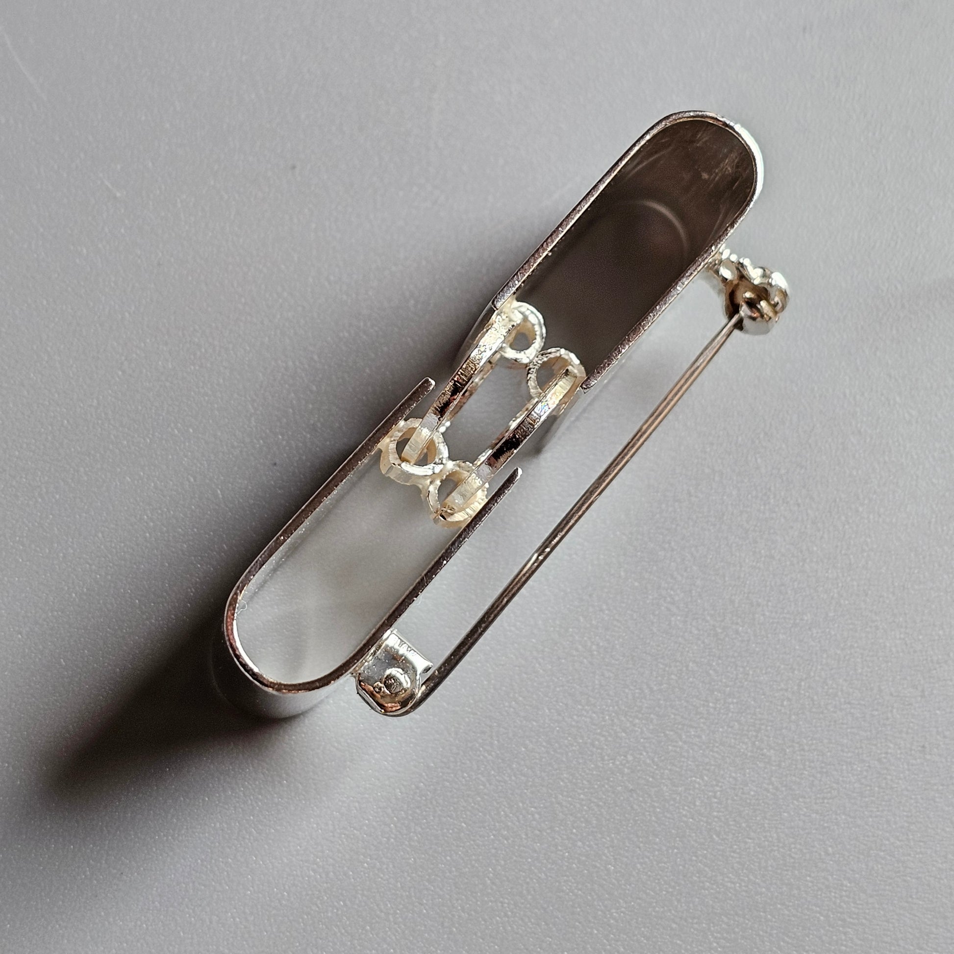 Silver safety pin with a decorative element on its clasp.