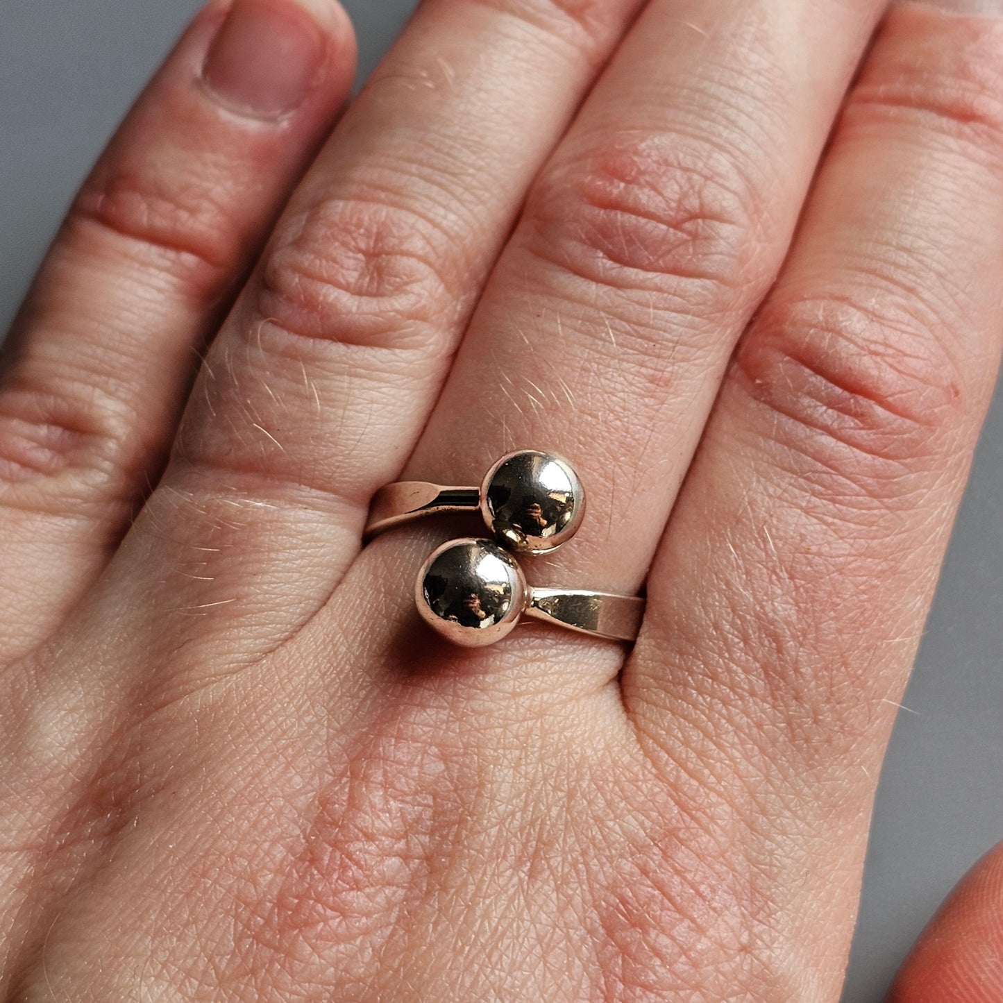 Silver ring with two spherical beads worn on a finger.