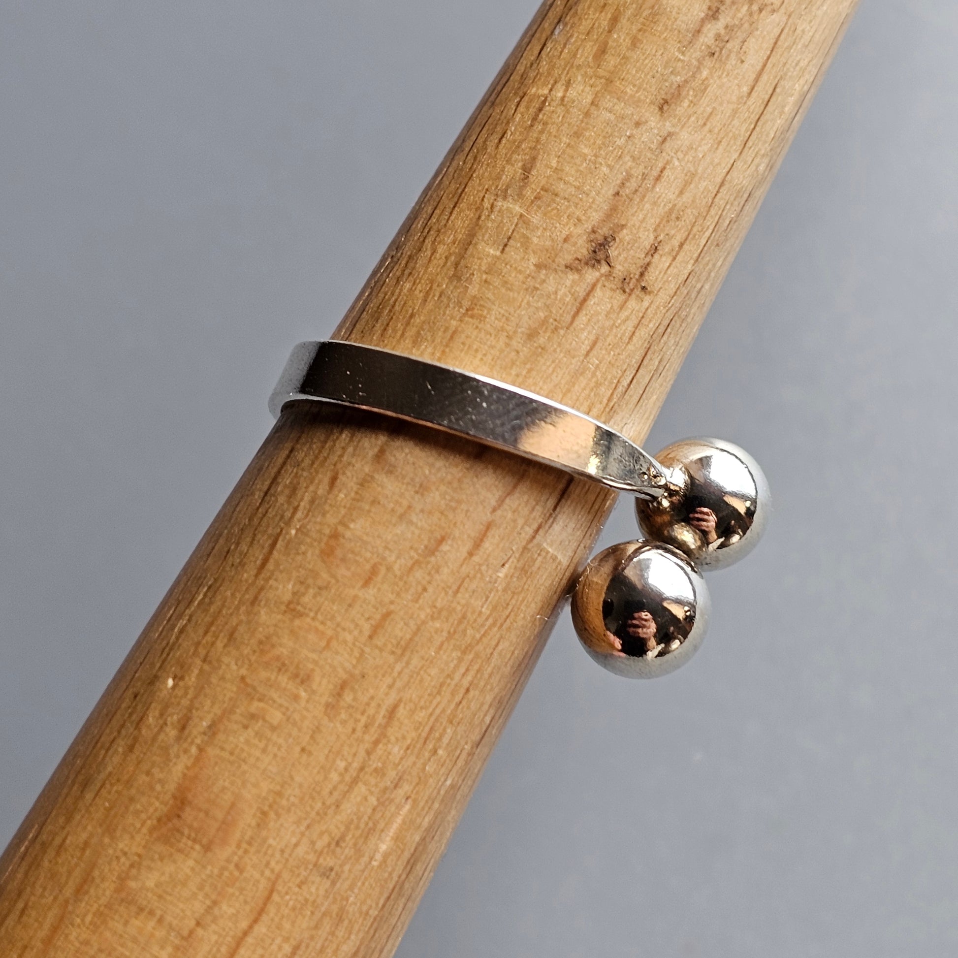 Silver ring with two small spherical charms attached to the band.