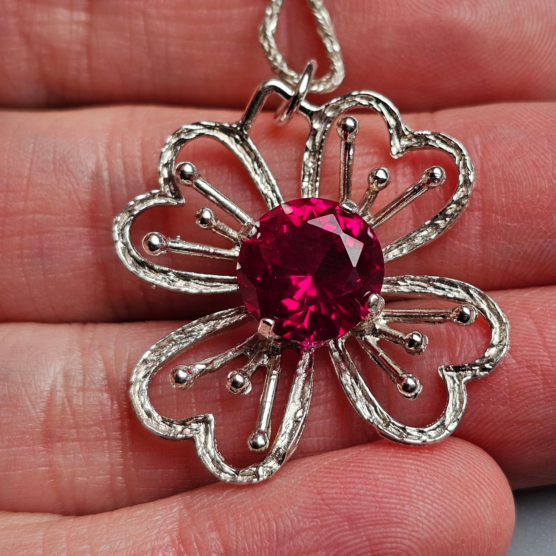 Silver flower-shaped pendant with a vibrant red gemstone center.