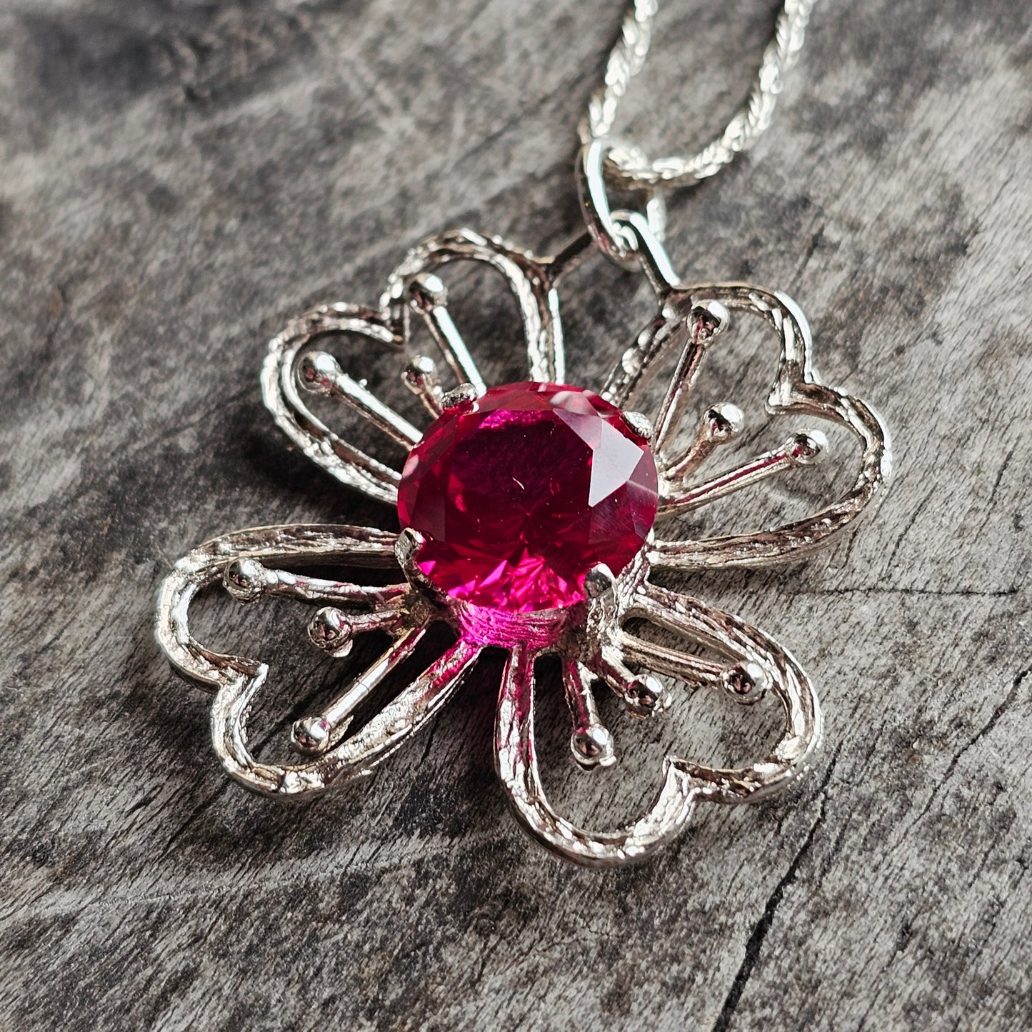 Silver flower-shaped pendant with a vibrant pink gemstone center.