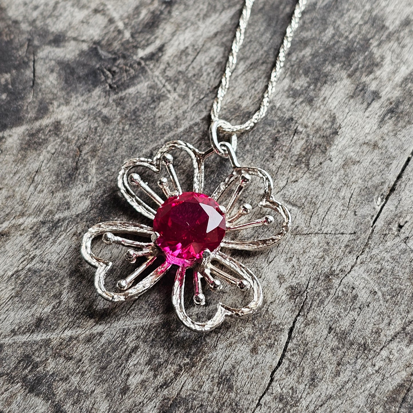 Silver flower-shaped pendant with a vibrant pink gemstone center on a chain.