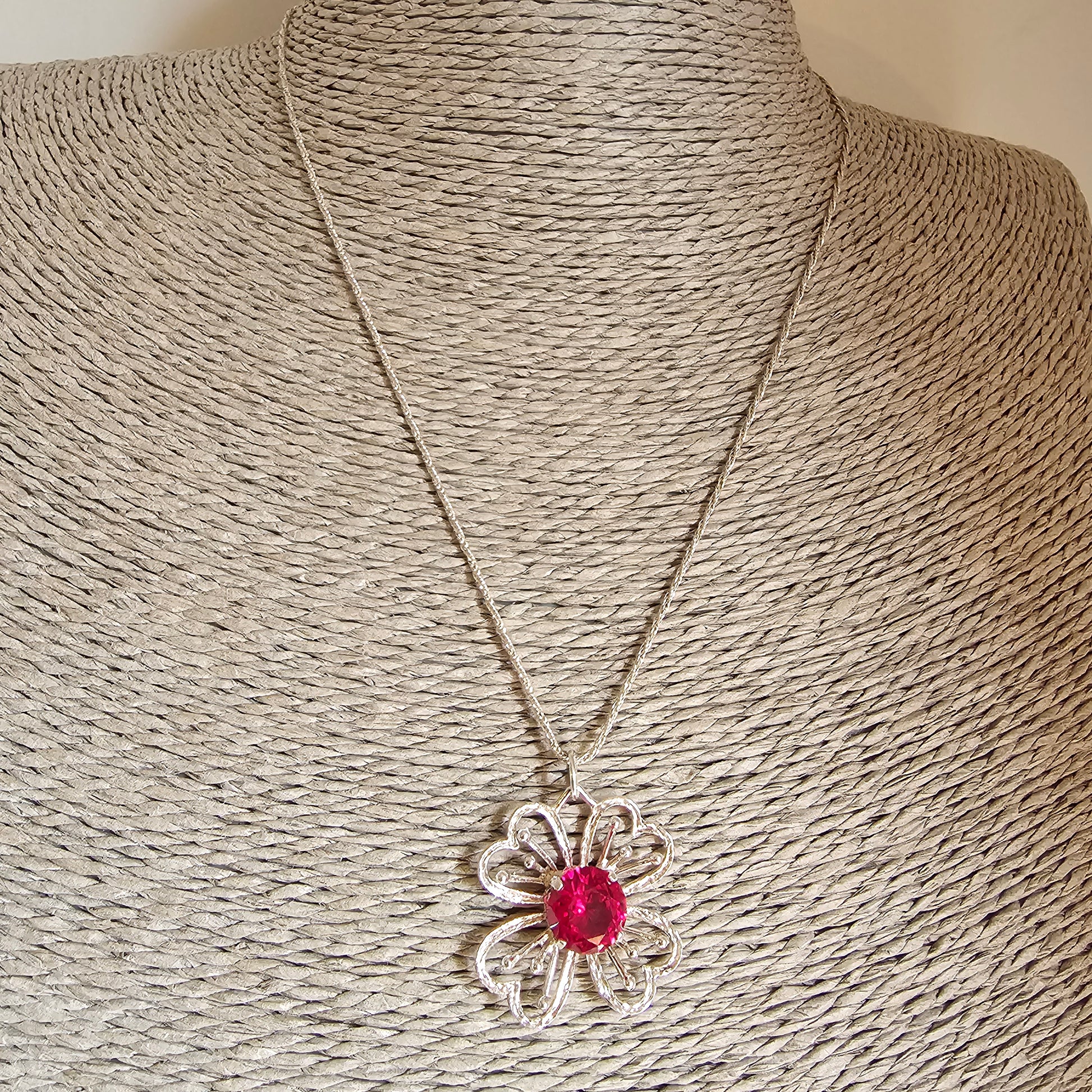 Silver flower-shaped pendant necklace with a red gemstone center.