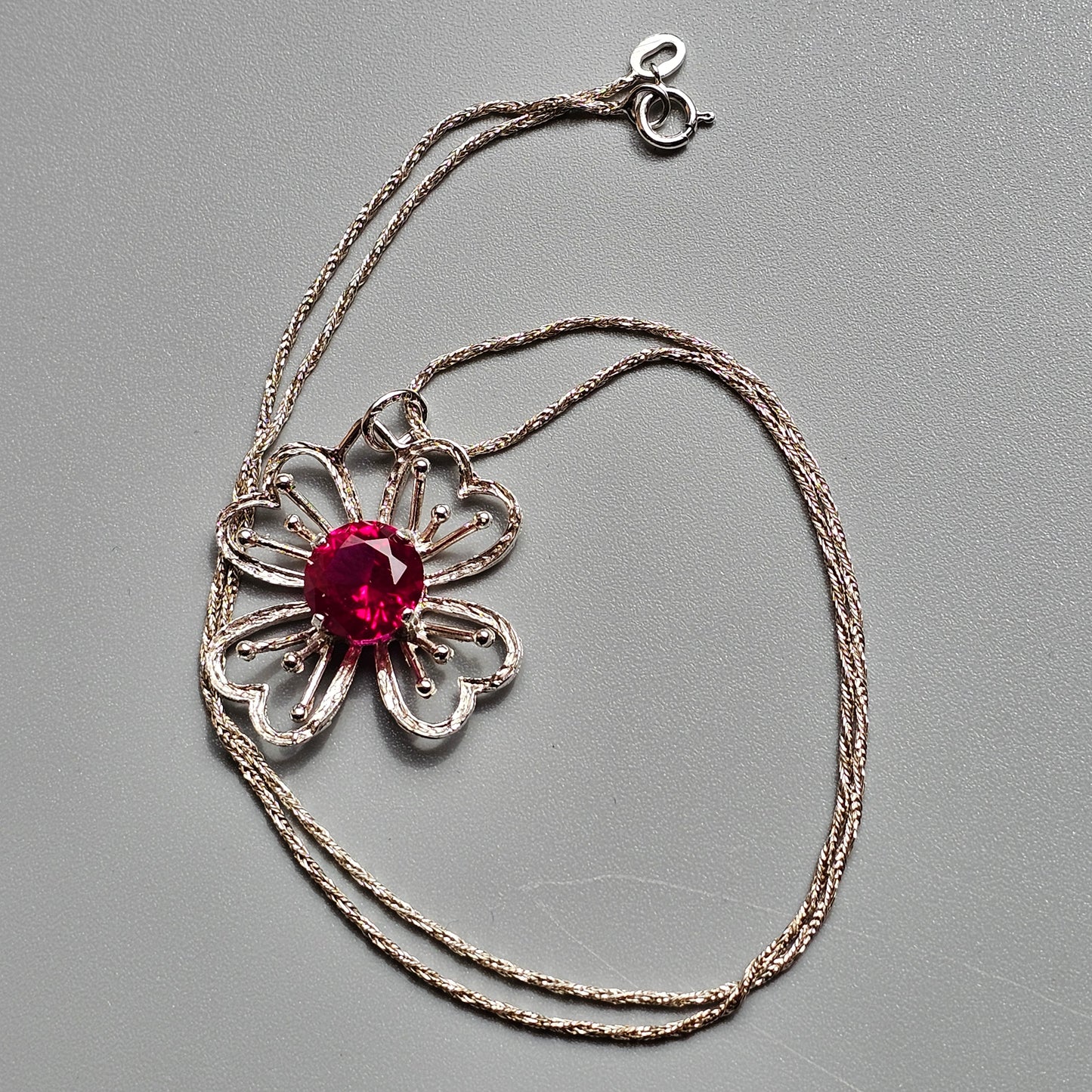 Silver flower-shaped pendant necklace with a red gemstone center.