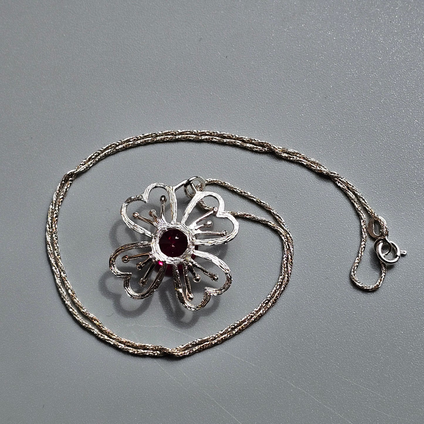 Silver flower-shaped pendant with a red gemstone center on a delicate chain necklace.