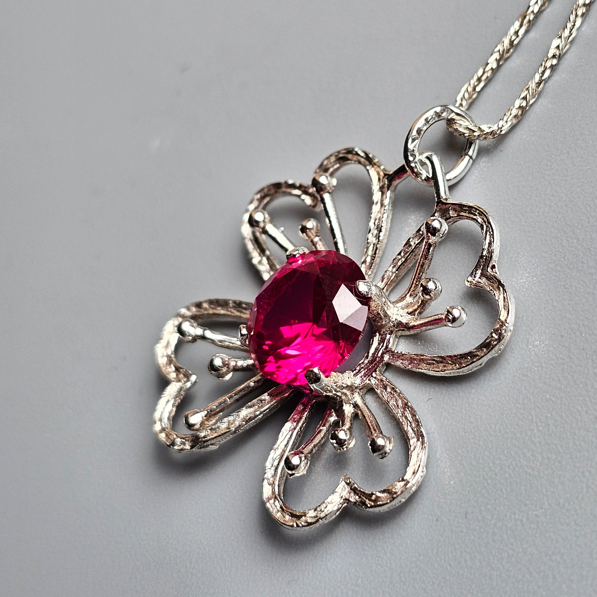 Flower-shaped silver pendant with a vibrant pink gemstone center.