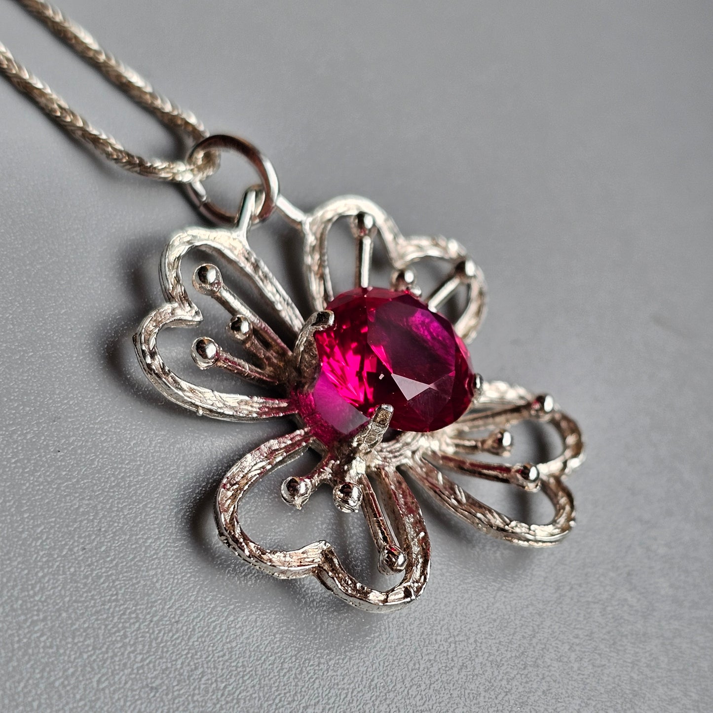 Silver flower-shaped pendant necklace with a vibrant pink gemstone center.