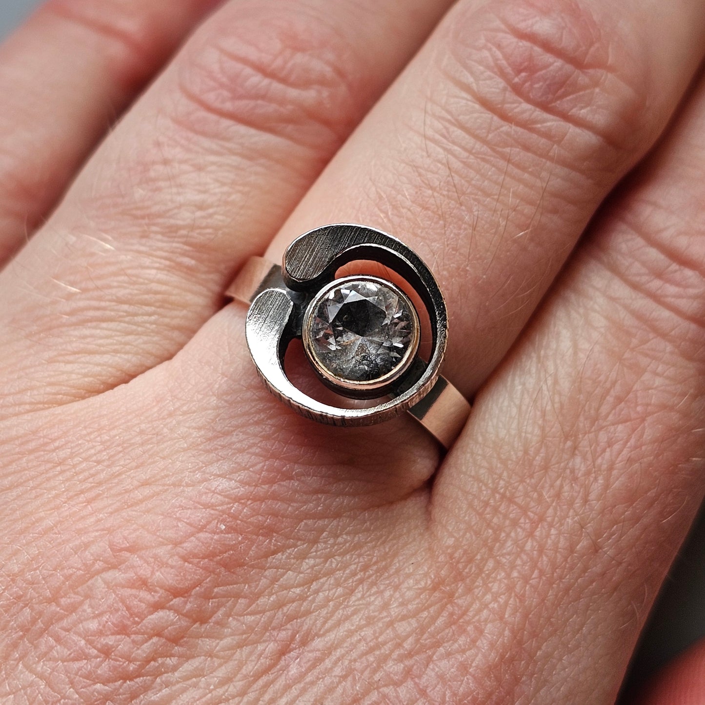 Modern silver ring with a circular design featuring a central clear gemstone.