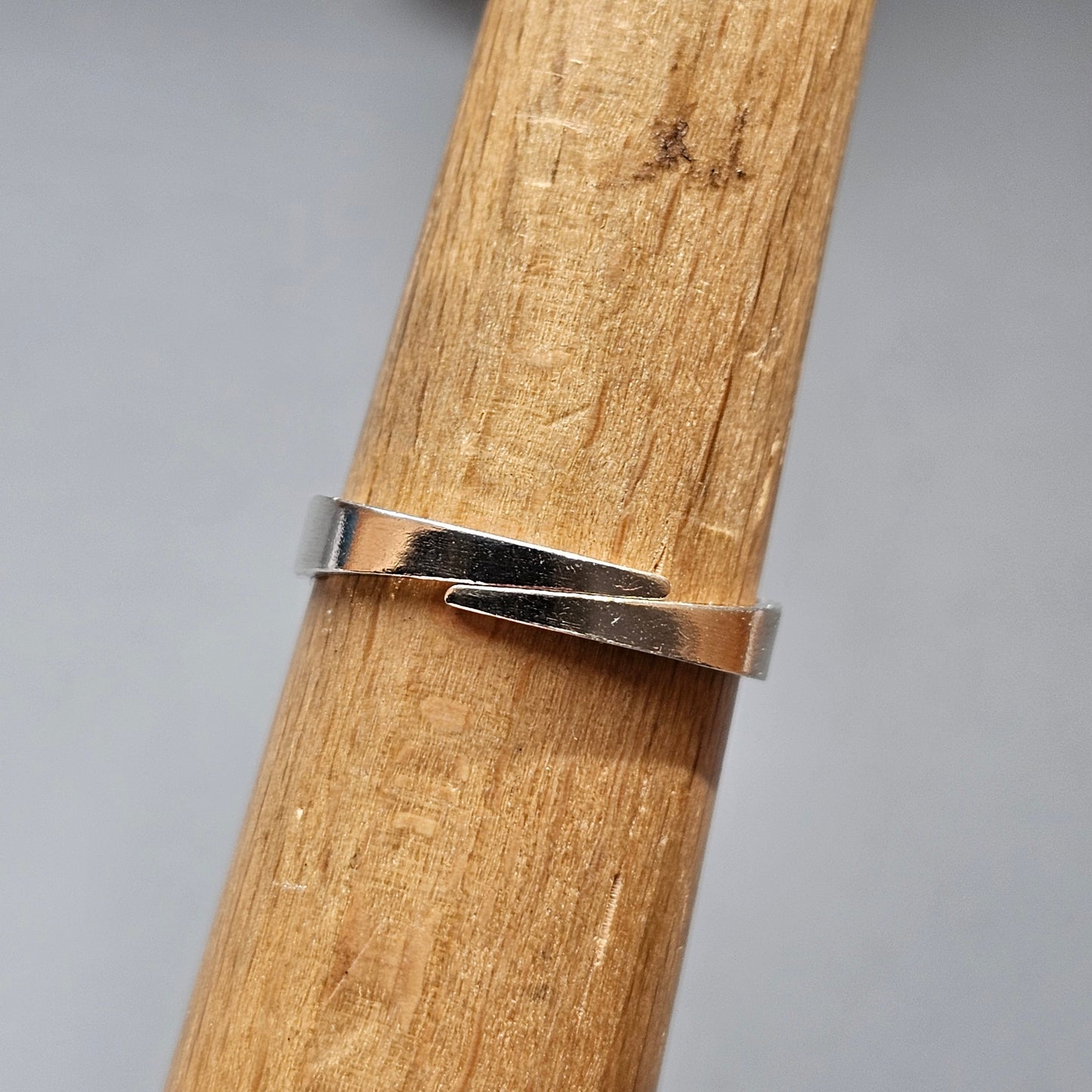 Silver ring with a twisted or overlapping design wrapped around a wooden surface.