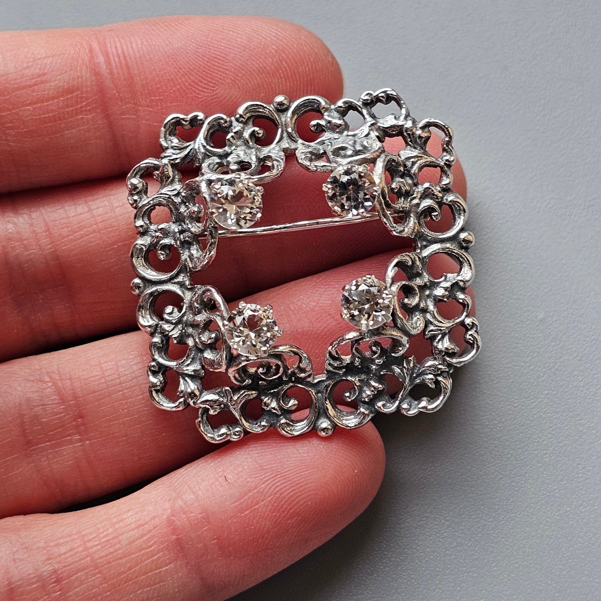 Ornate silver brooch with intricate scrollwork and rhinestone accents.