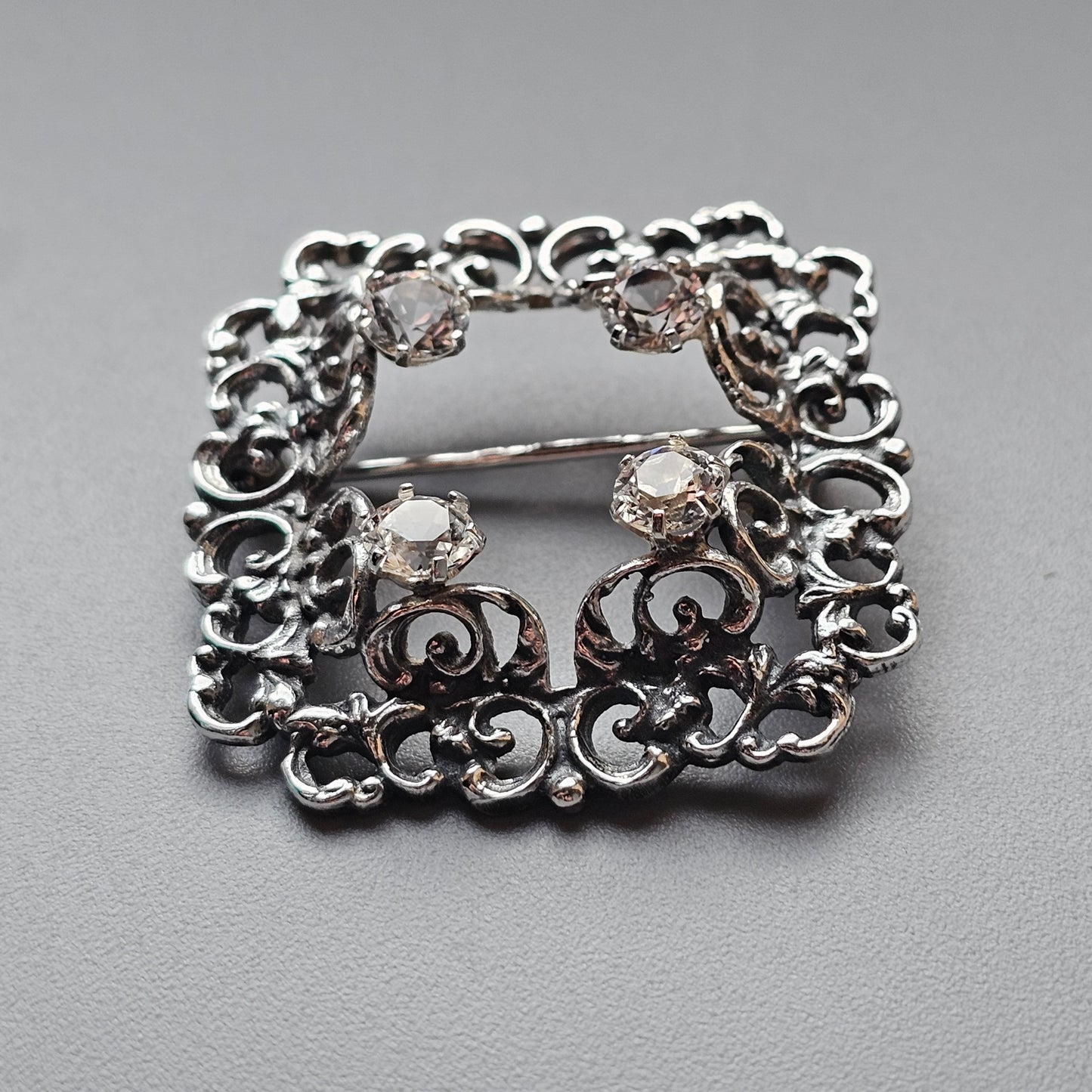 Ornate silver brooch with intricate scrollwork and gemstones.