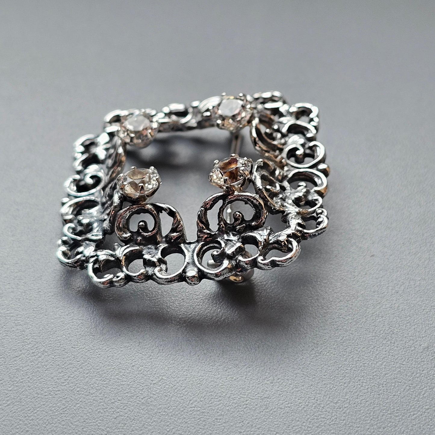 Ornate silver brooch with intricate scrollwork and small gemstones.