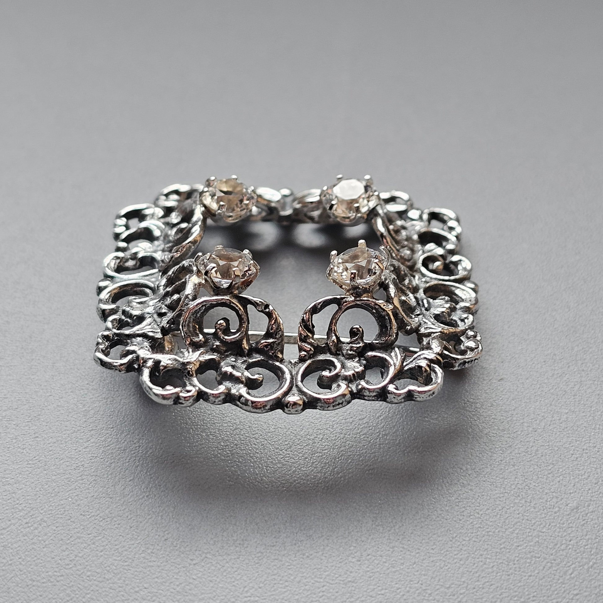 Ornate silver brooch with intricate filigree design and gemstone accents.